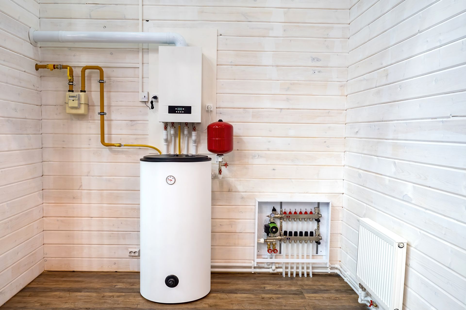 A white home heating system with a water tank, boiler, and manifold installed on a wooden wall in a utility room.