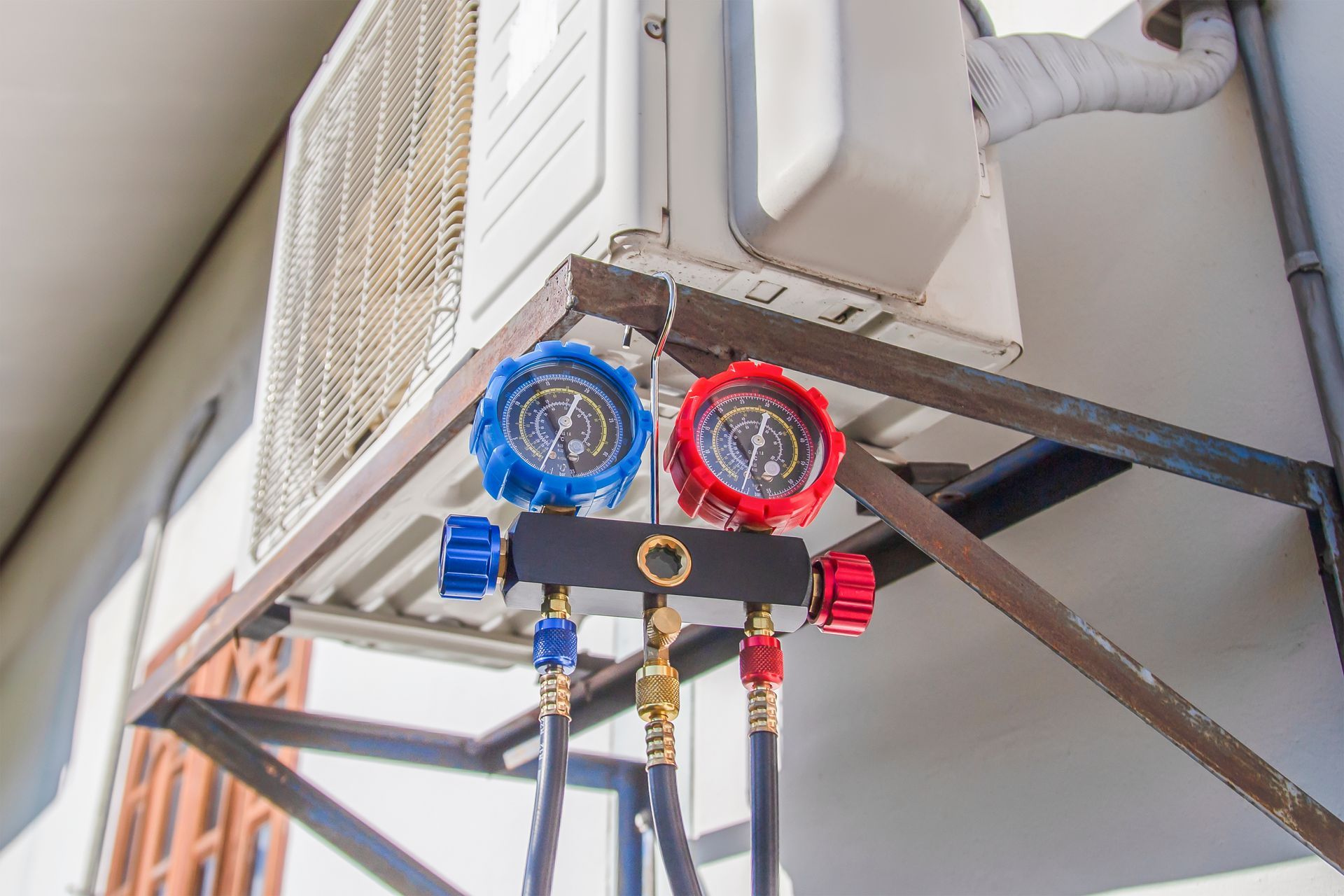 Manifold gauge set with blue and red dials attached to the outdoor unit of a residential air conditioning system.