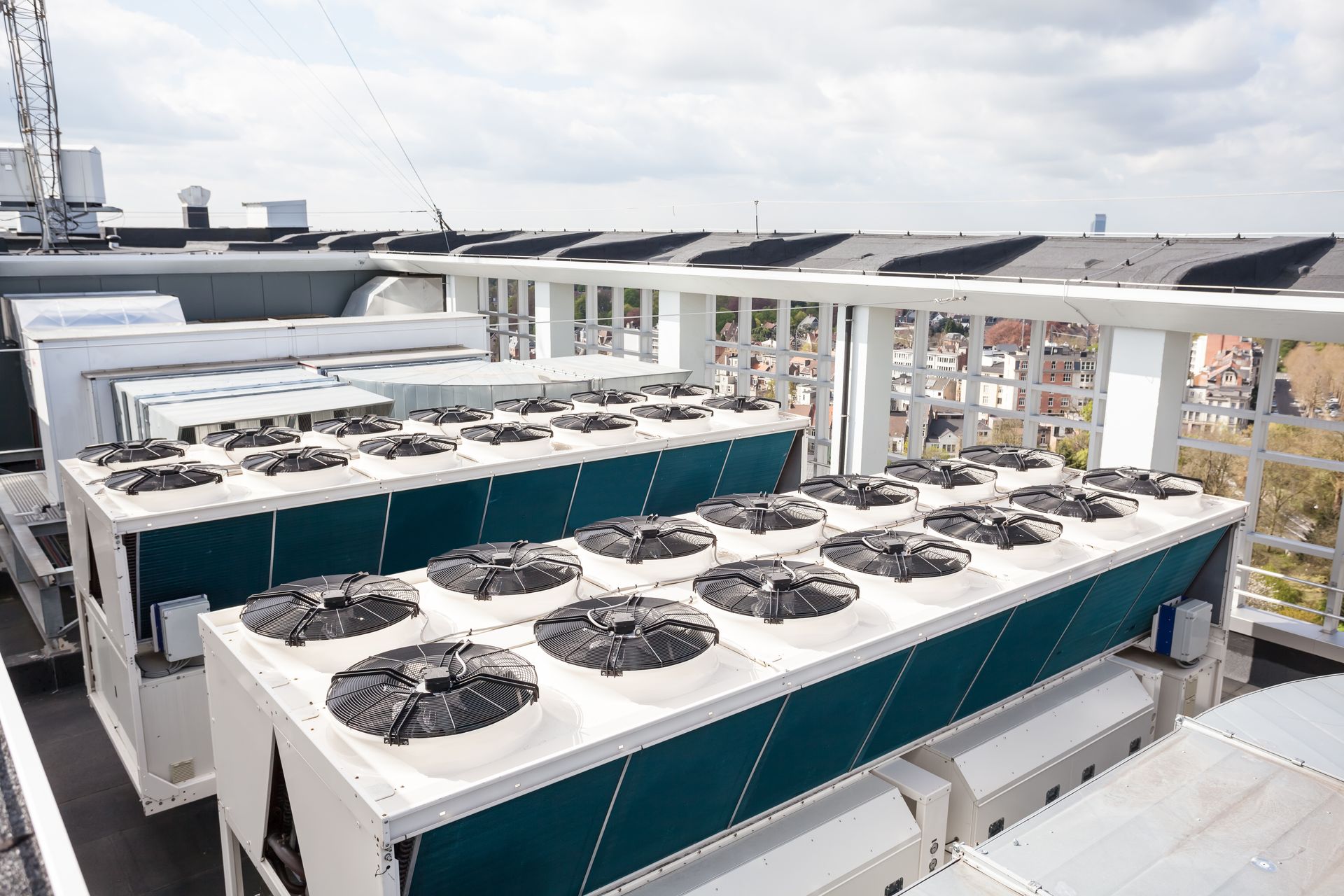 Multiple large, industrial rooftop HVAC air conditioning units with visible circular fans, set against a cloudy sky.