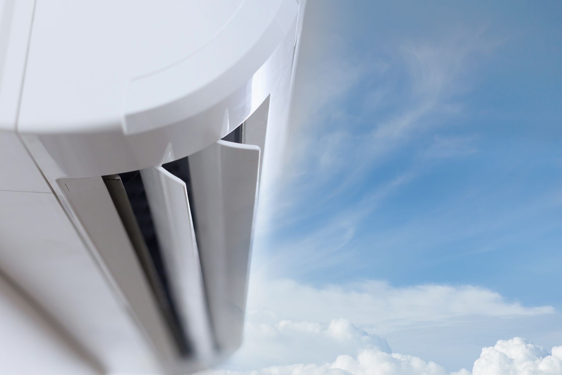 A close-up of a white wall-mounted air conditioner unit positioned against a bright, cloudy blue sky.