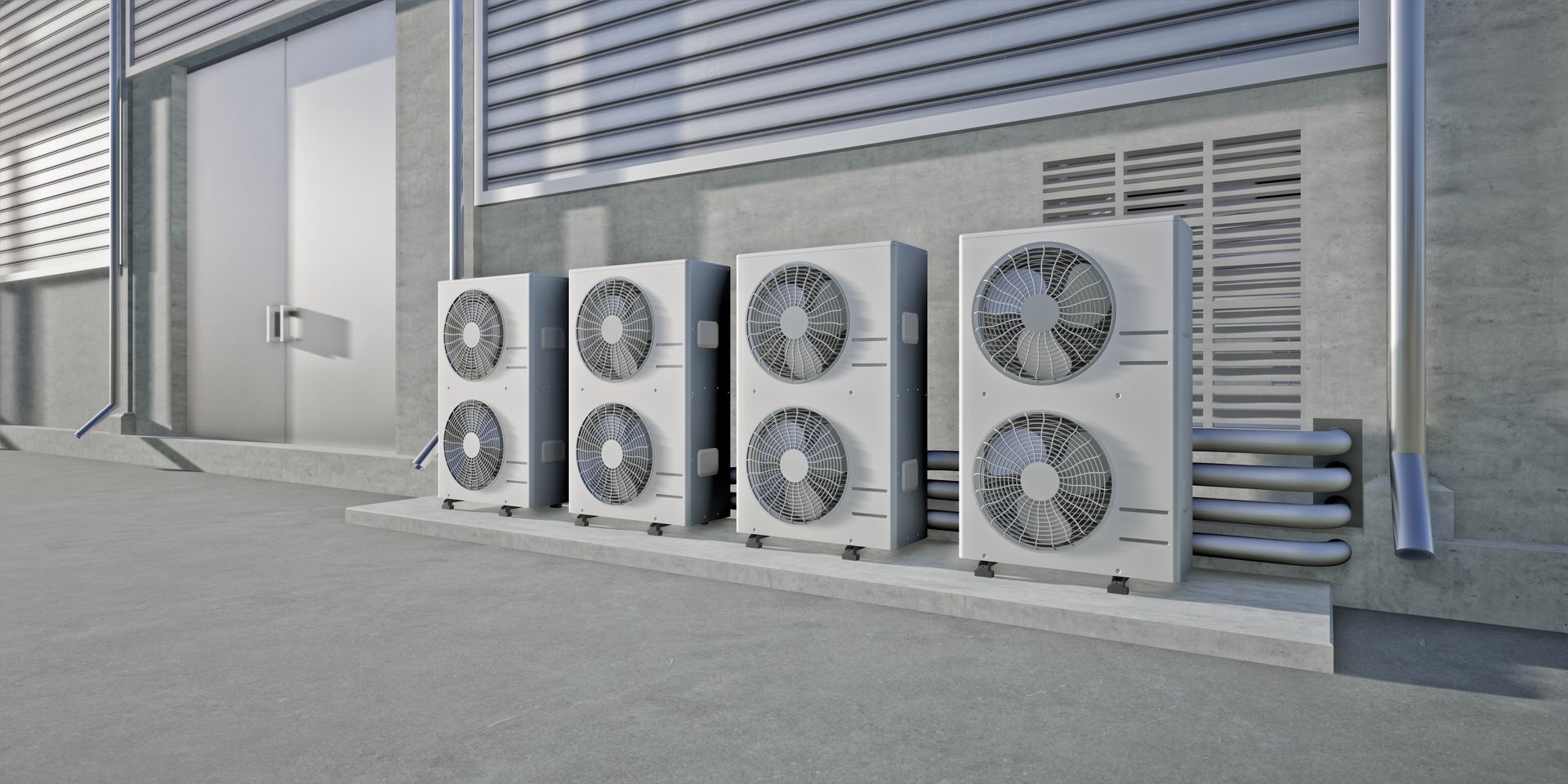 Four grey outdoor air conditioning units lined up against the side of a modern industrial building.