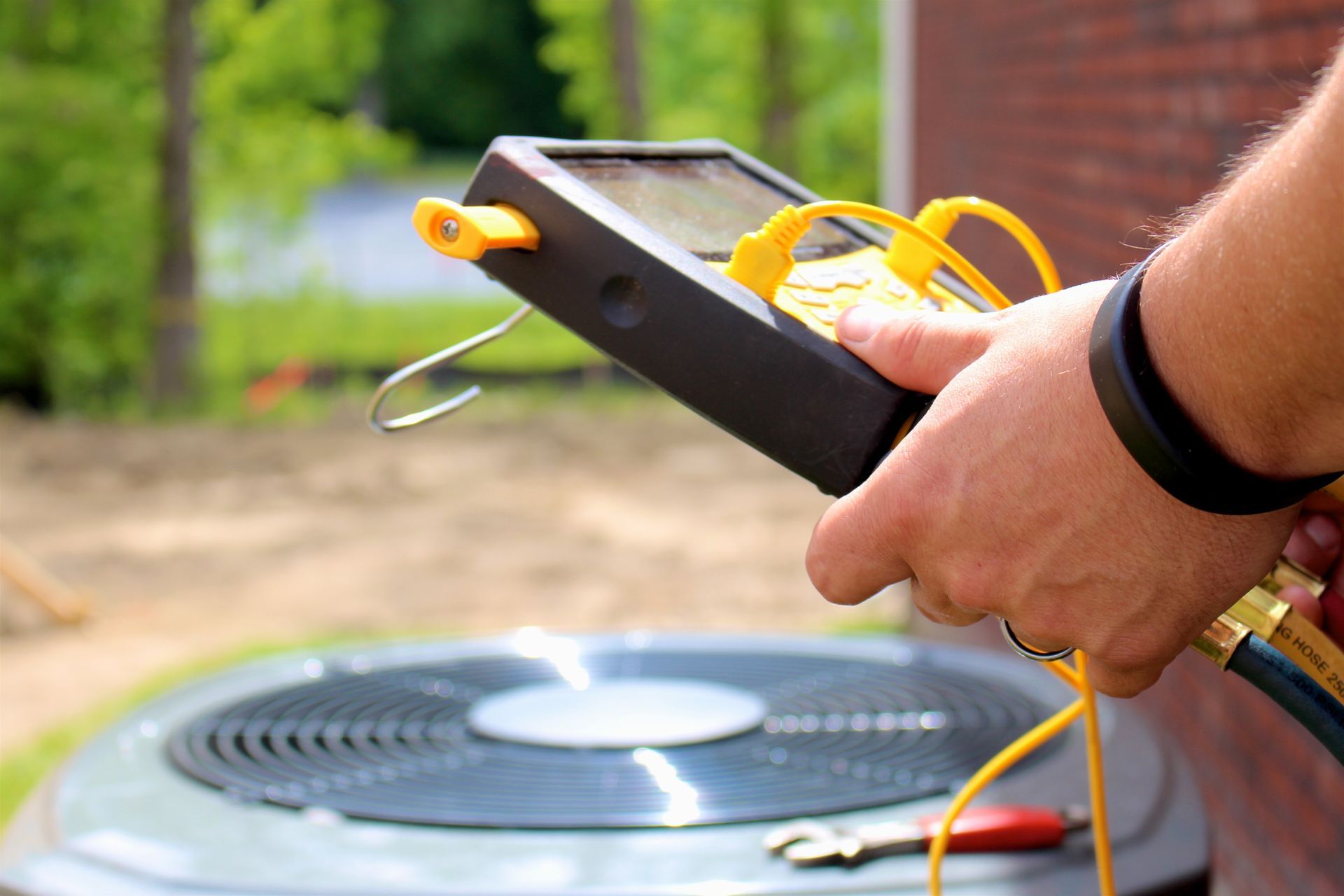 Technician holding a digital diagnostic gauge connected to an outdoor HVAC condenser unit.