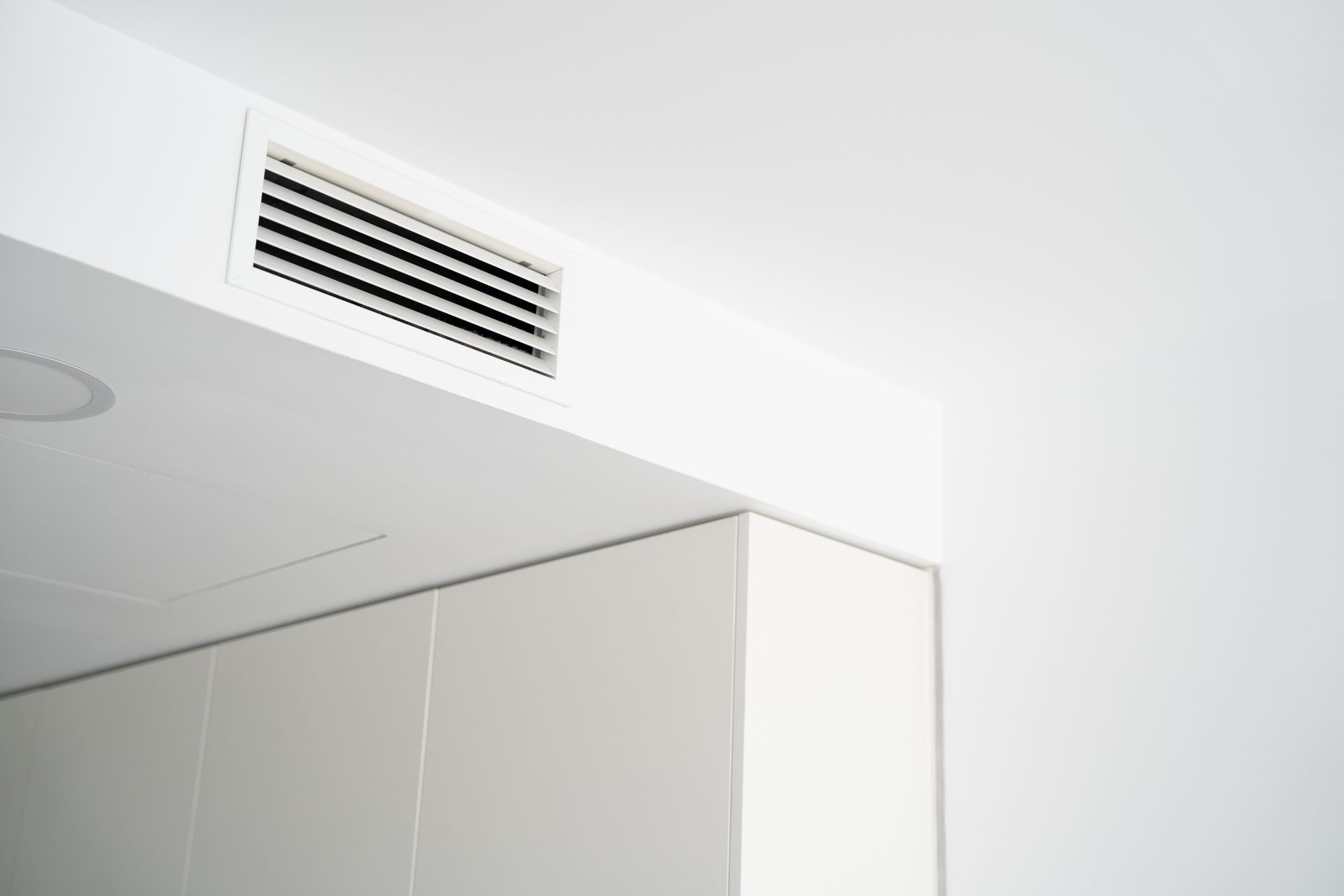 A modern white ceiling vent integrated into a room corner above white cabinetry.