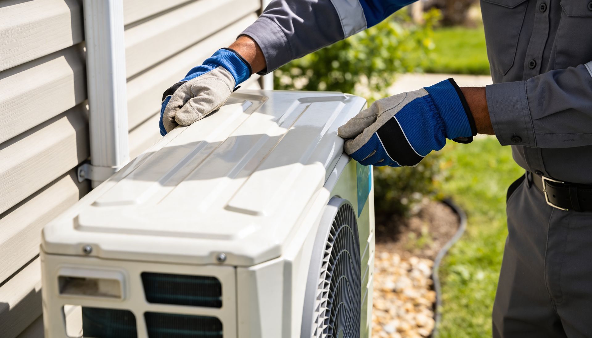 A technician wearing work gloves performs maintenance on an outdoor residential air conditioning unit.