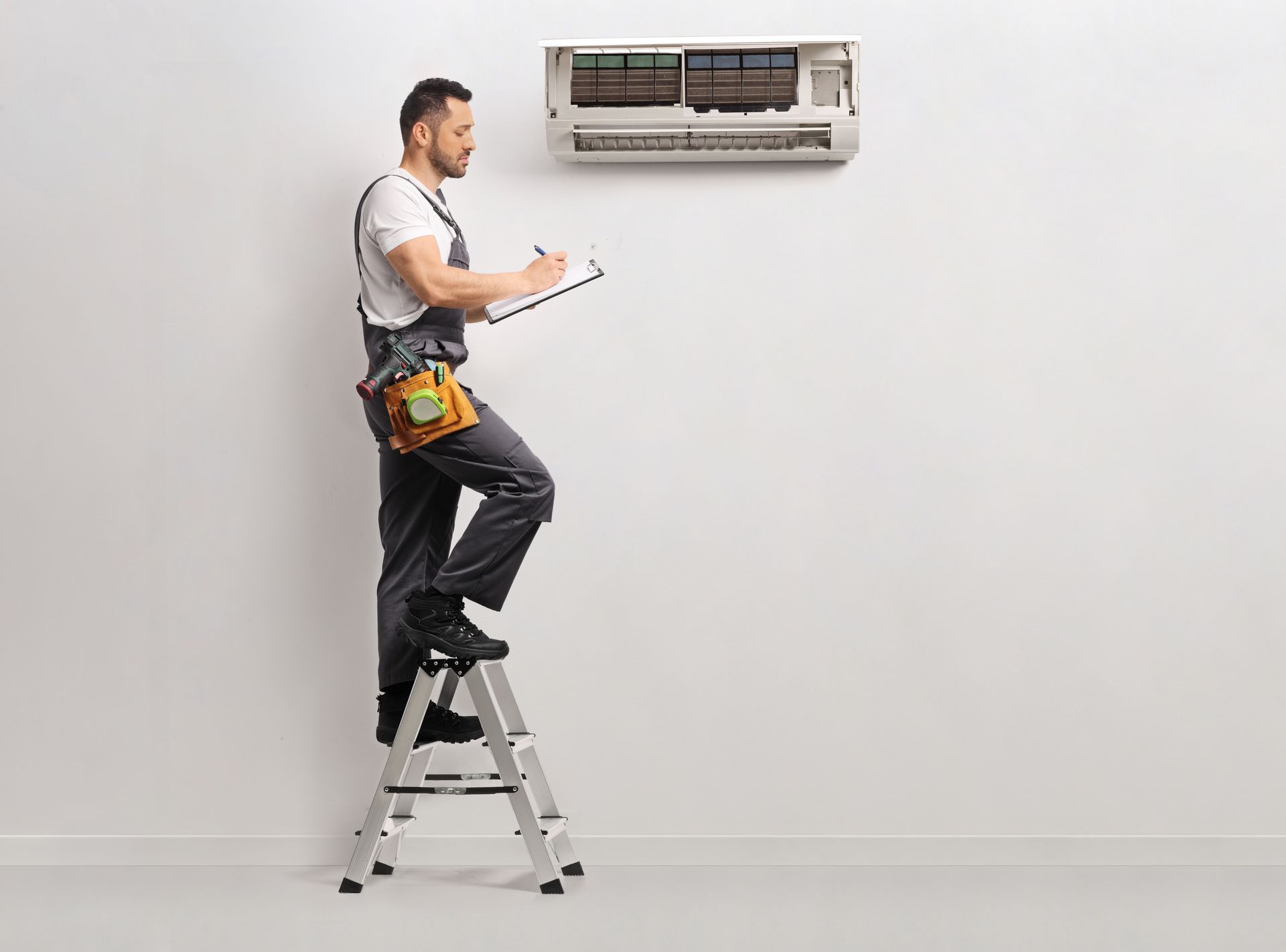 An HVAC technician inspecting a wall-mounted mini-split AC unit while standing on a ladder