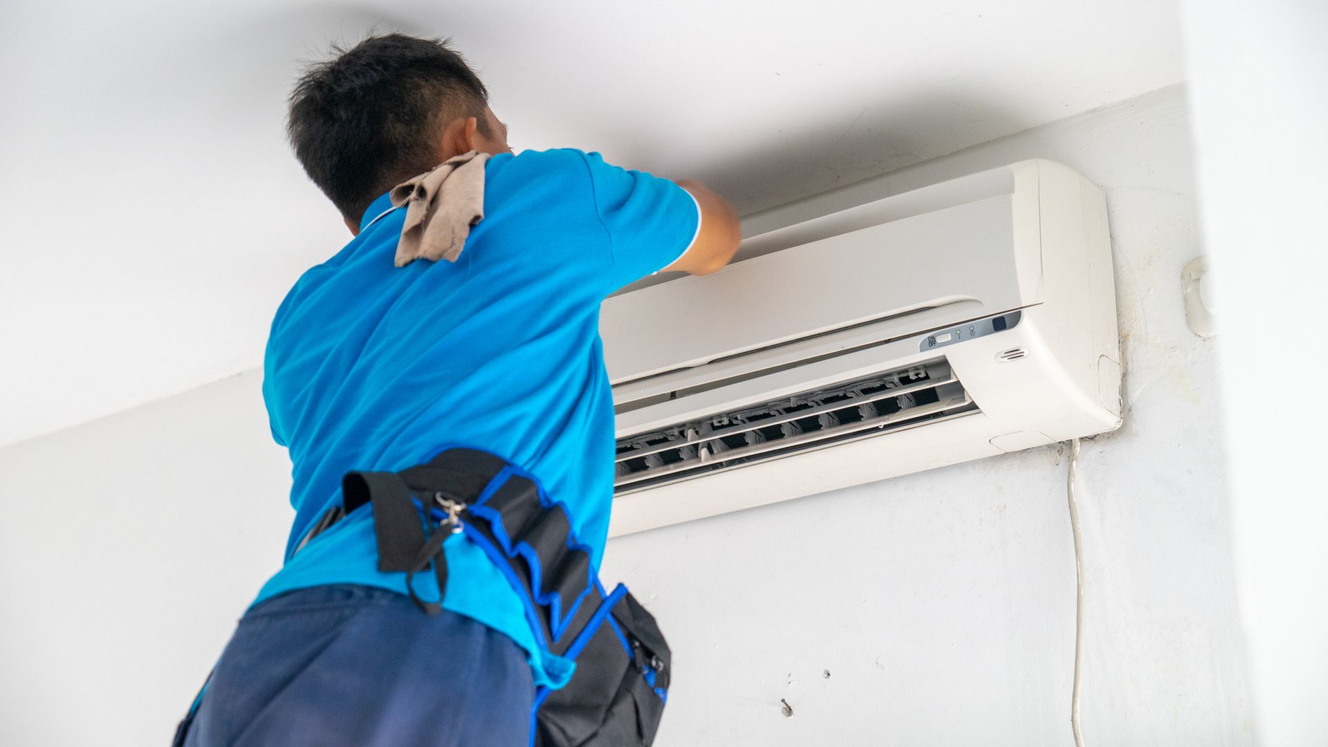 An HVAC technician servicing a wall-mounted split-system air conditioner unit indoors