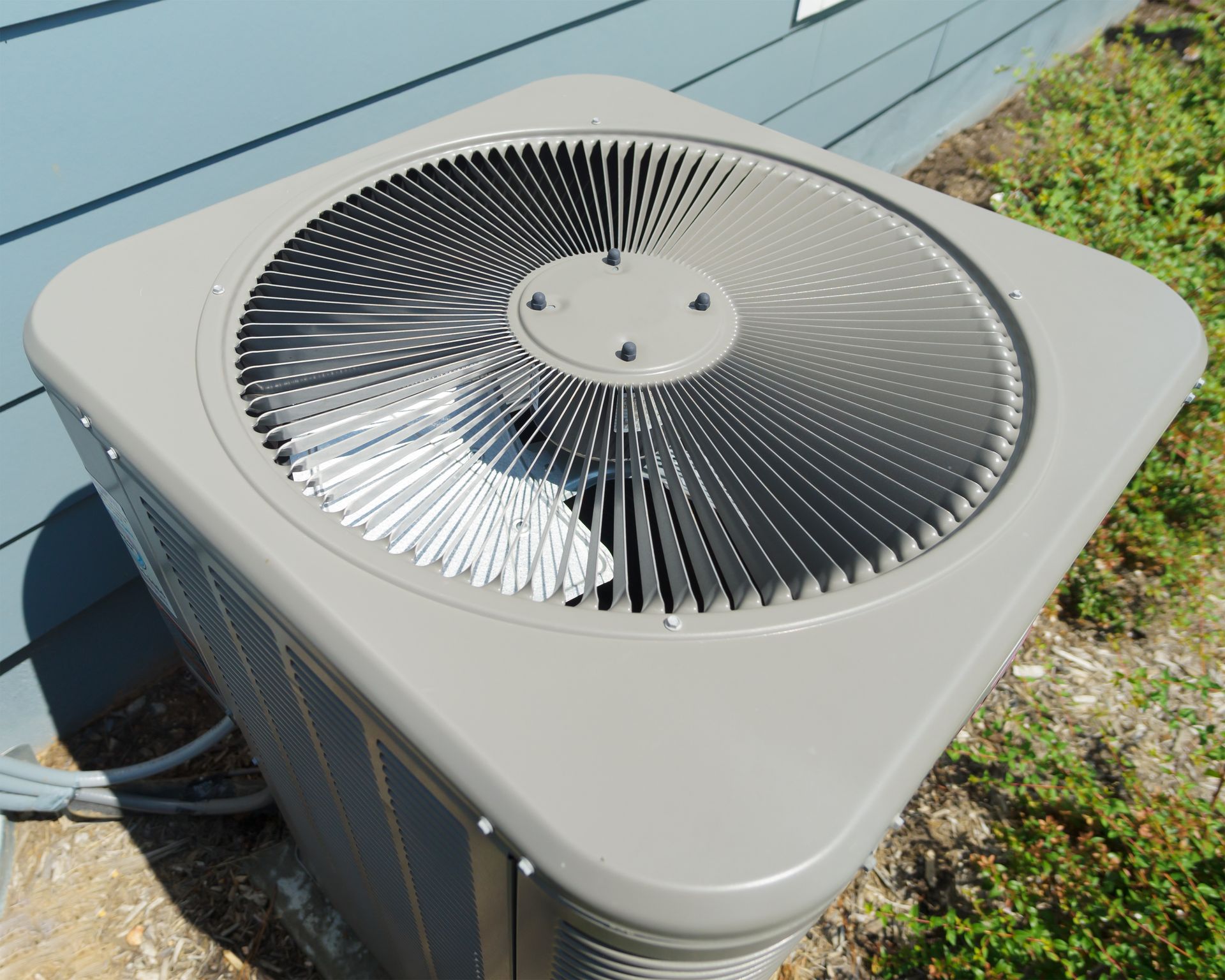 A light gray residential HVAC air conditioning unit sitting outside against a blue-sided house.