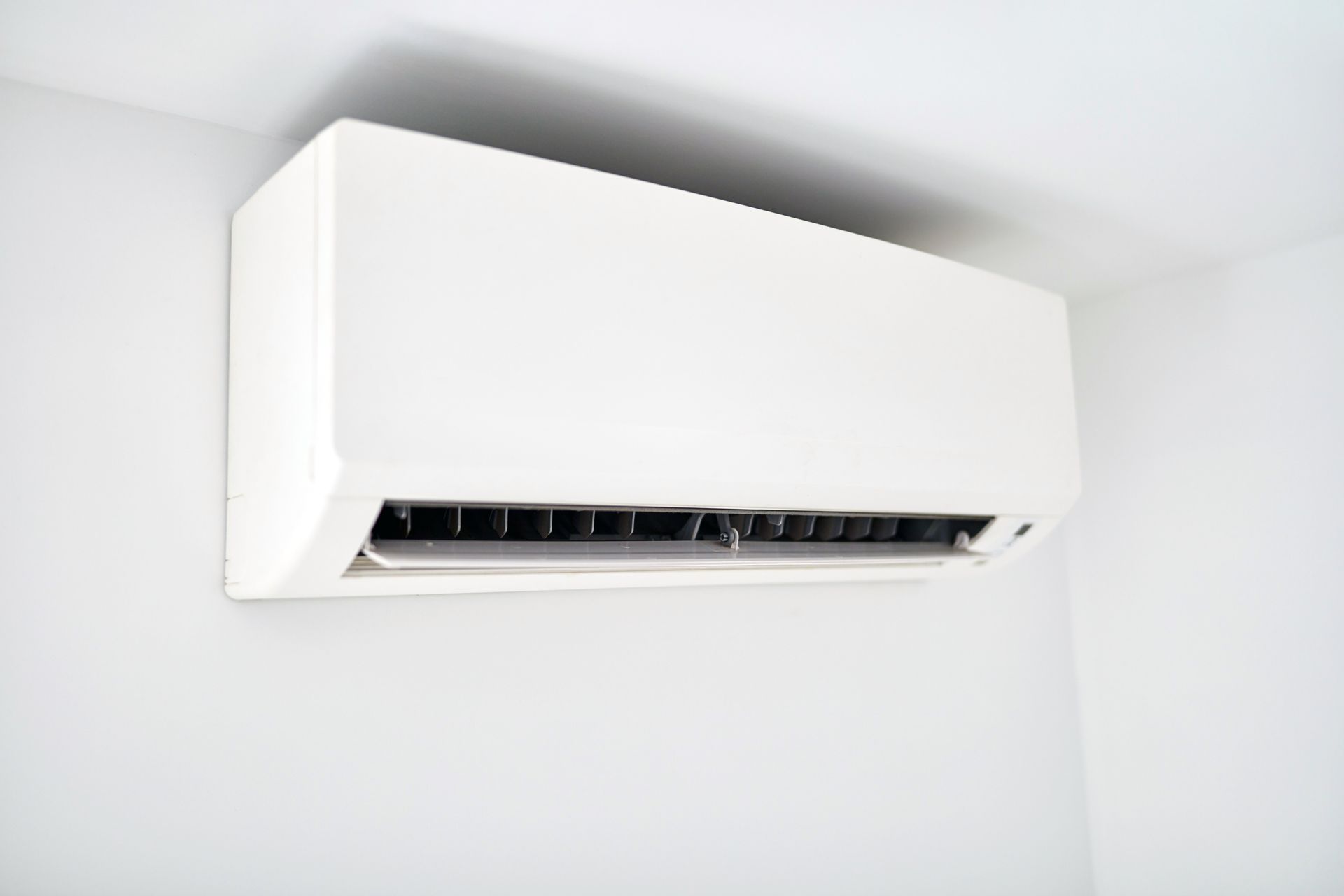 A white wall-mounted air conditioner unit installed near the ceiling against a plain white wall.