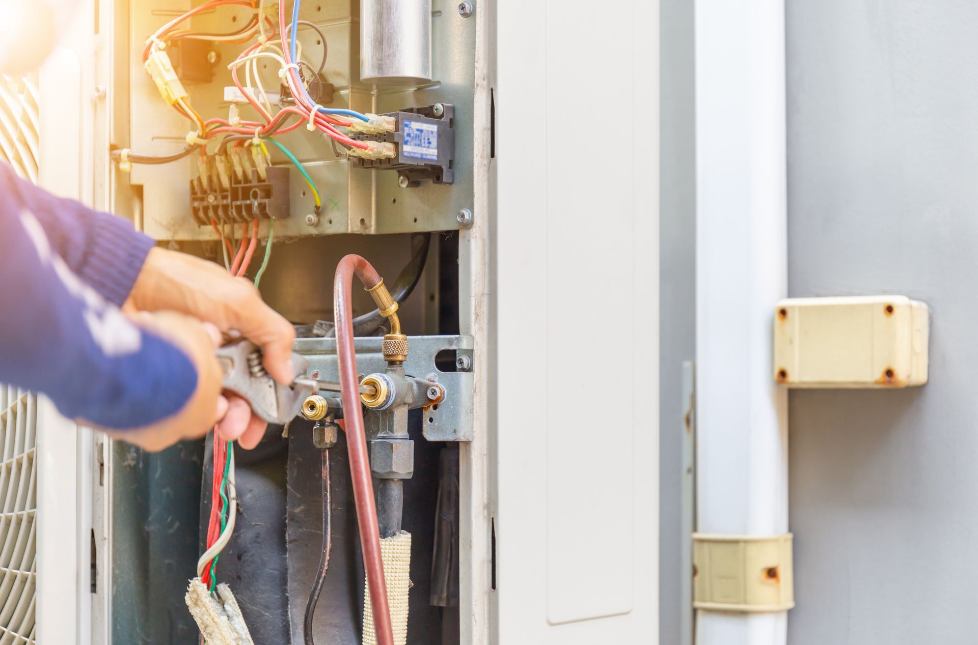 A technician using a wrench to repair the internal components and copper pipes of an outdoor air conditioning unit.