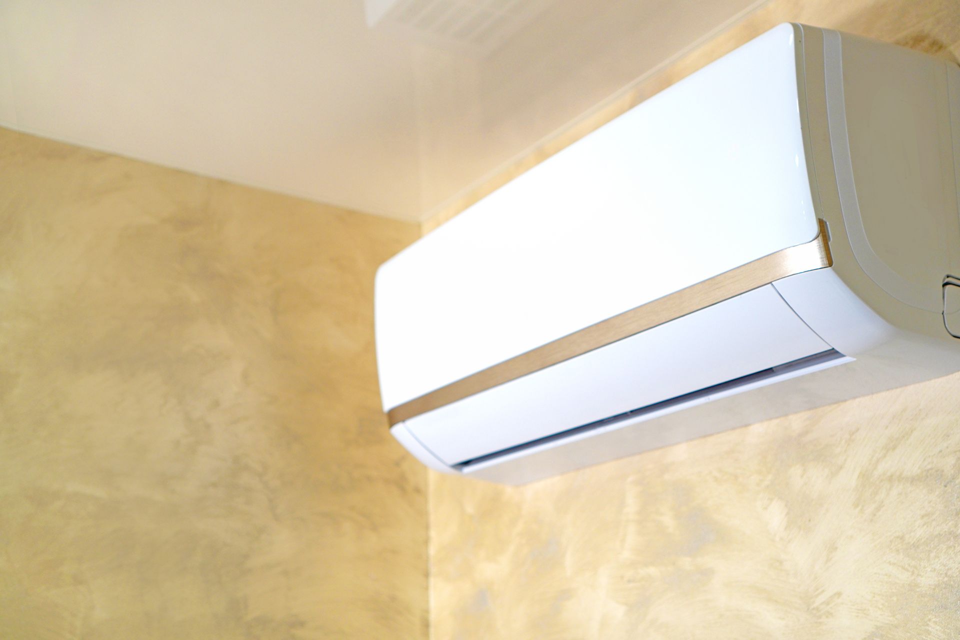 A white wall-mounted air conditioning unit installed in the corner of a room with textured tan walls.