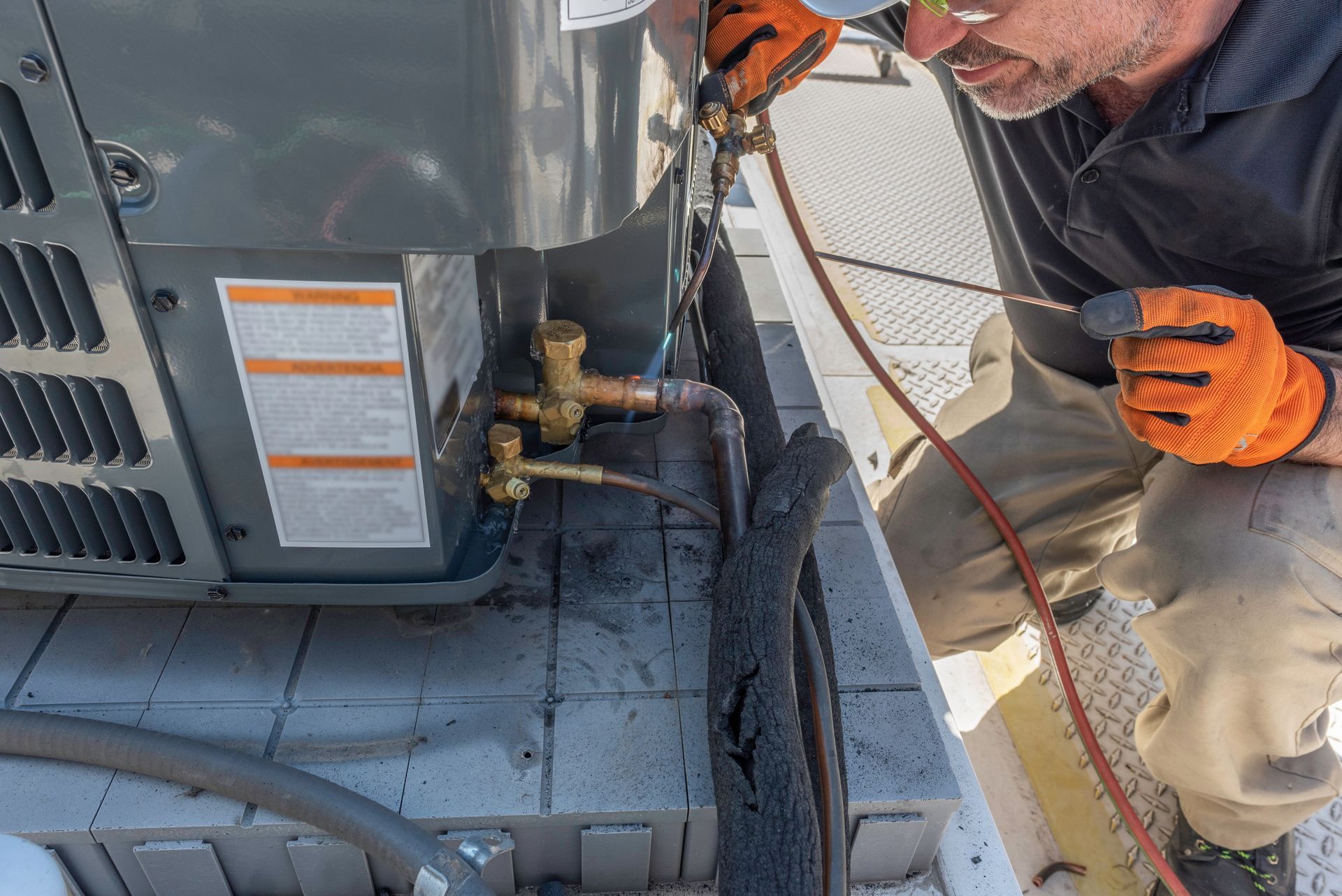 A technician uses a wrench to tighten the pipe connections on an outdoor air conditioning unit.