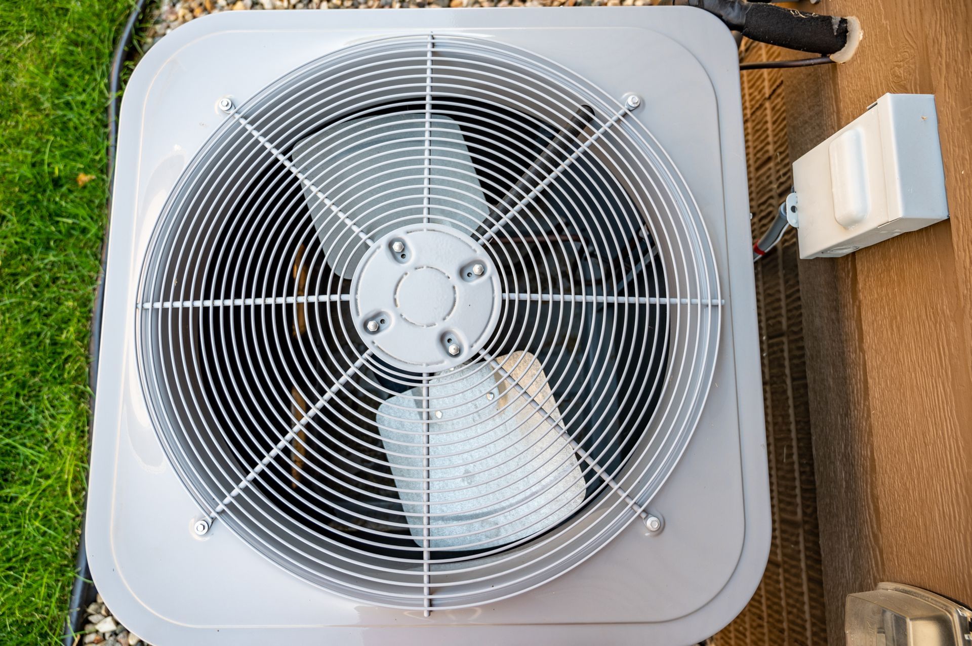 A top-down view of a grey residential air conditioning unit condenser with a circular protective metal fan grill.