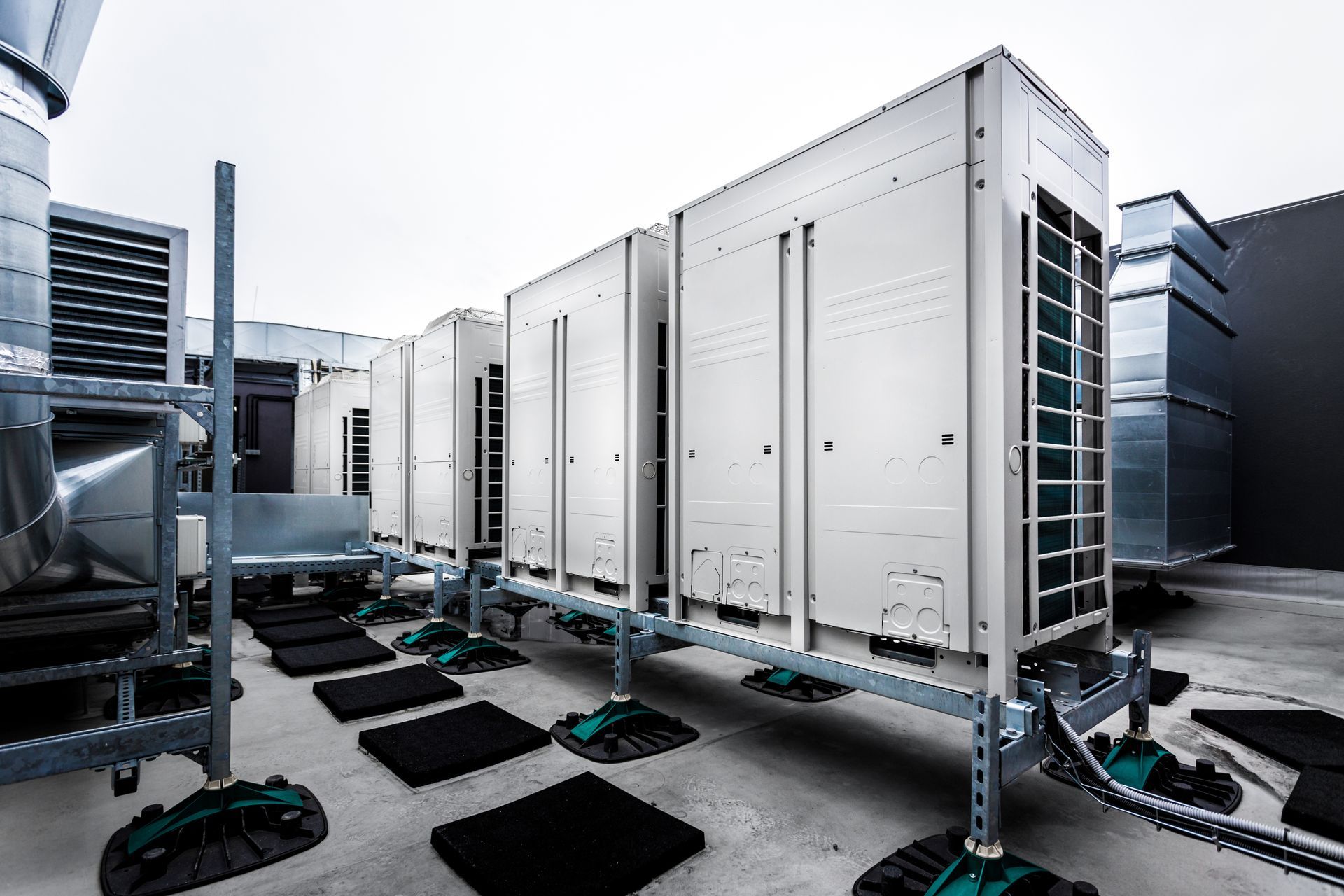 A row of modern HVAC outdoor units installed on a rooftop mounting system with black rubber vibration pads.