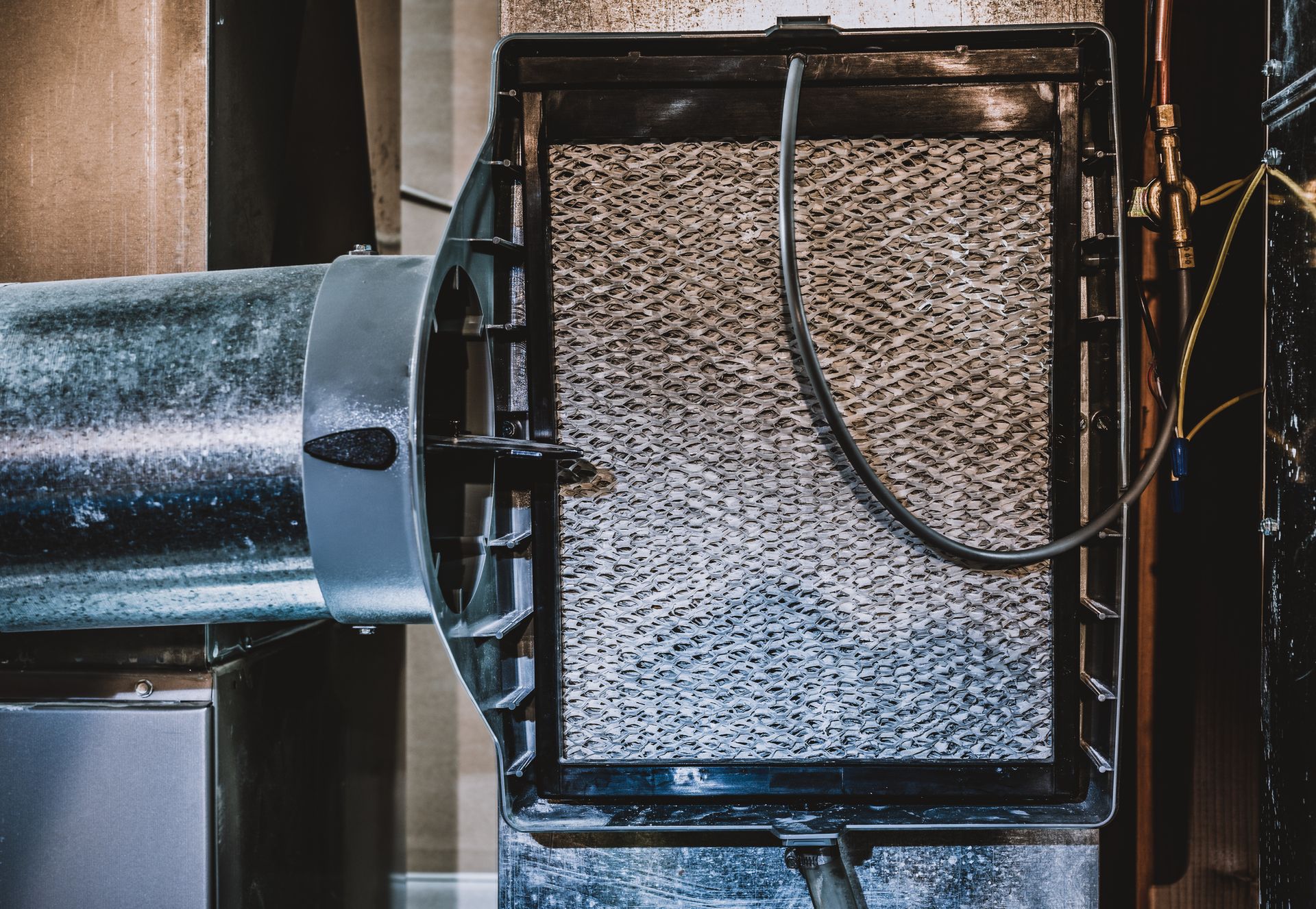 A close-up of a furnace humidifier pad mounted on a metal duct, featuring a textured, gray evaporation screen.