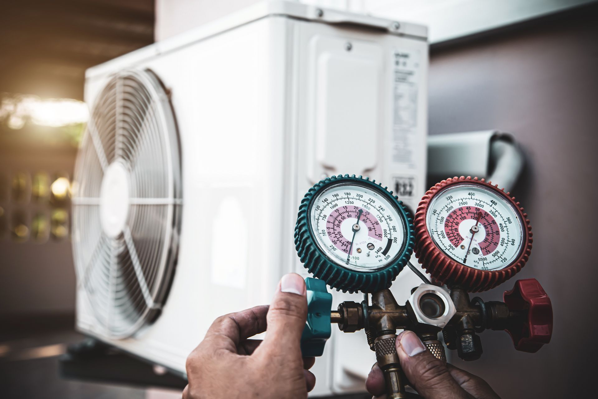 A technician's hands adjusting a manifold gauge set connected to an outdoor air conditioning condenser unit.