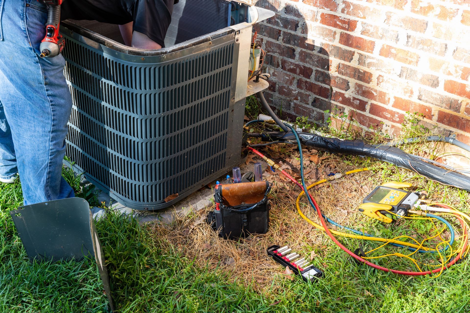 A service technician repairs an outdoor residential air conditioning unit next to a brick house.