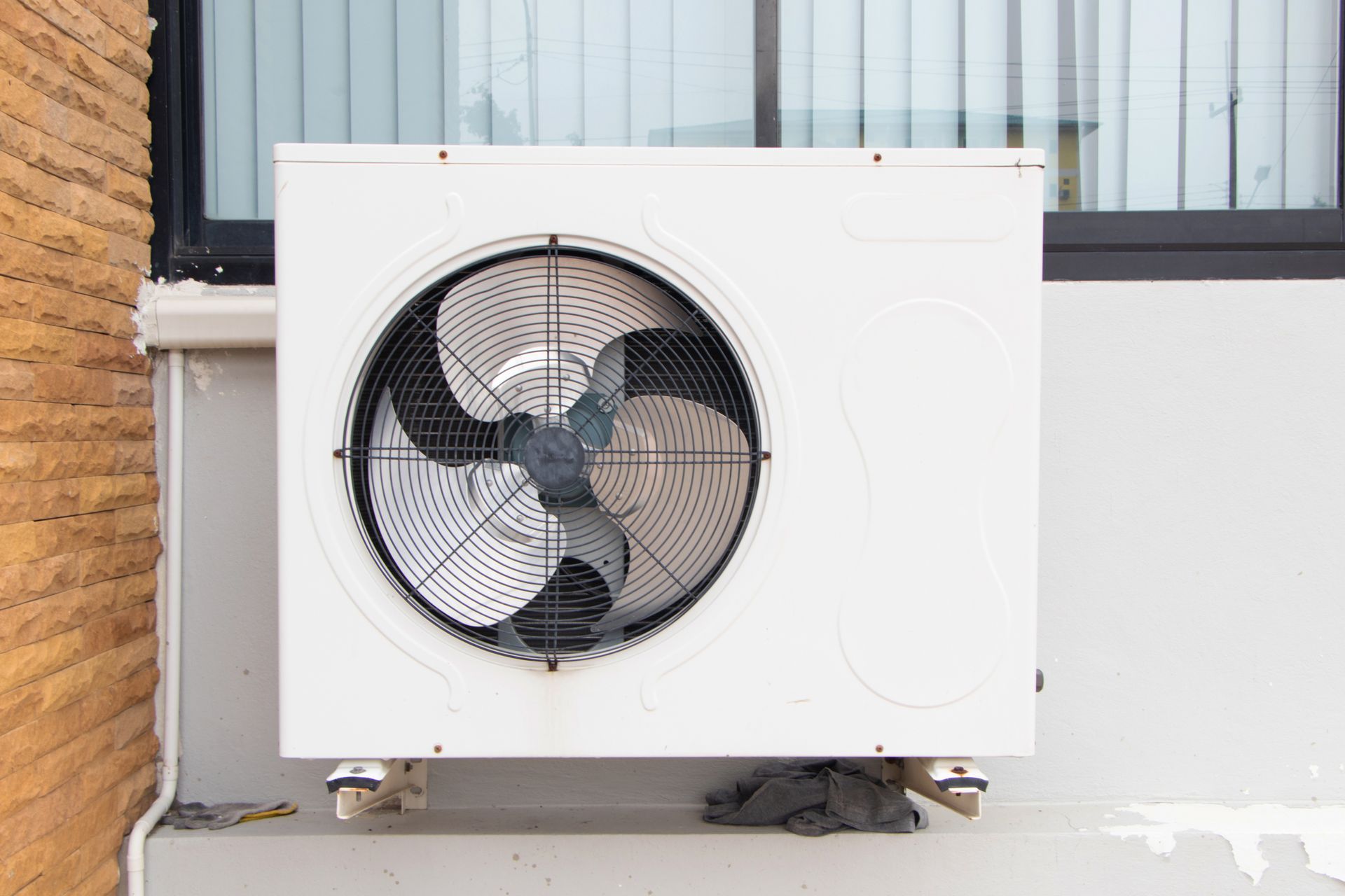 A white air conditioning condenser unit mounted on a wall against a building exterior.