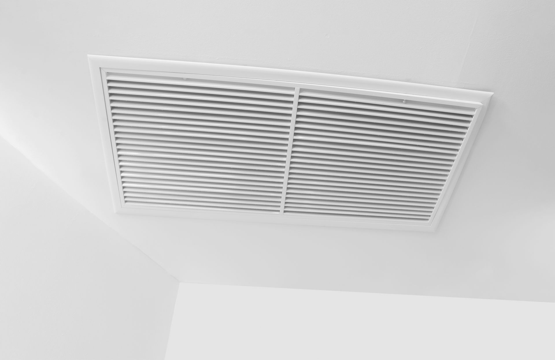 A white rectangular ceiling air vent with horizontal slats, installed on a white ceiling.