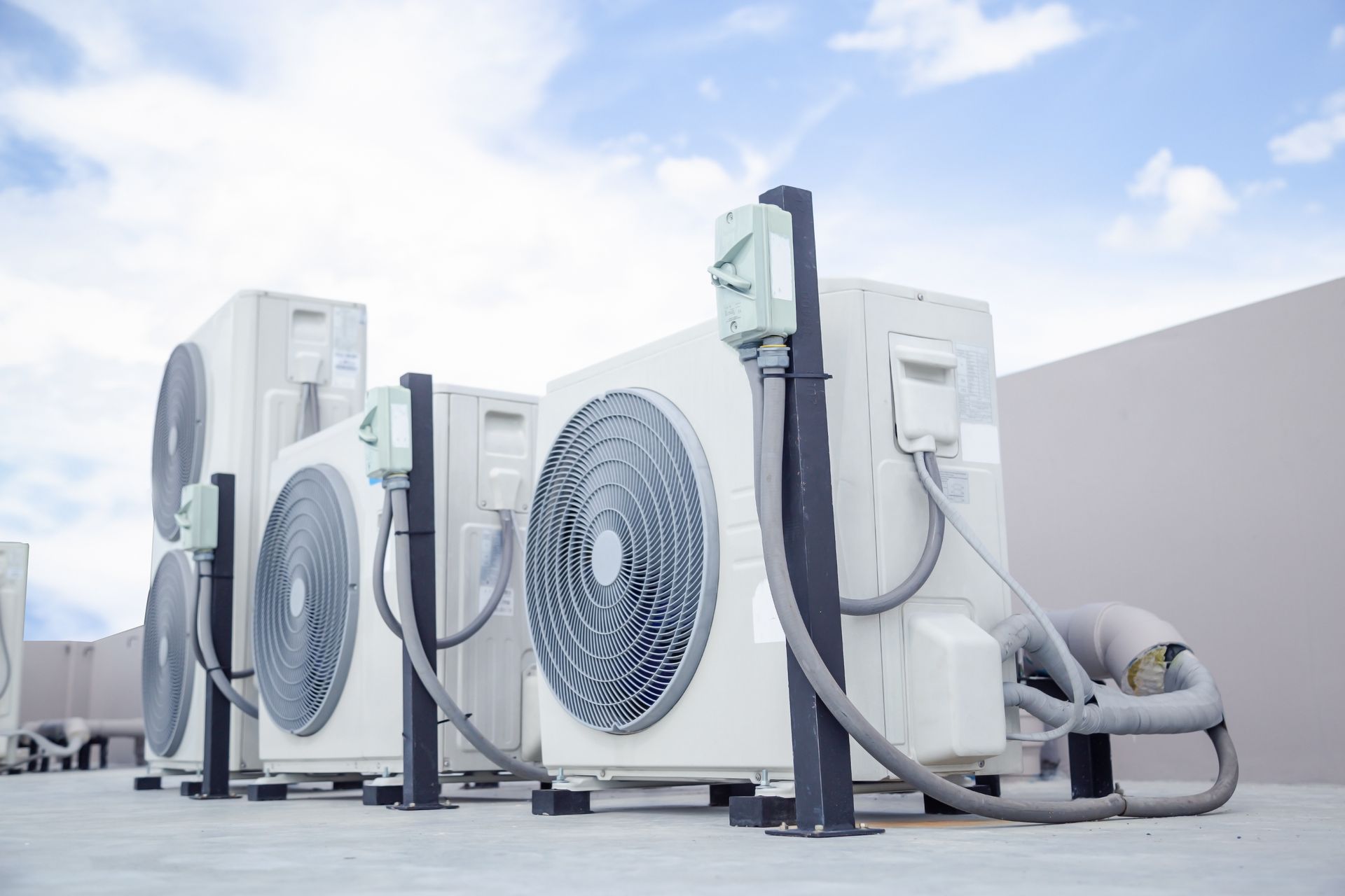 Three industrial HVAC outdoor condenser units on a rooftop against a cloudy blue sky.