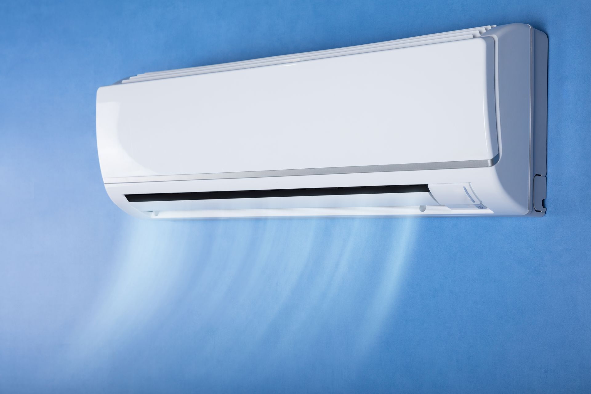 A wall-mounted white air conditioner emitting a cool breeze against a plain blue background.