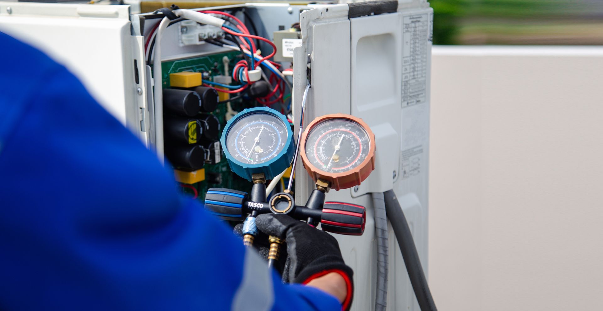 A technician in a blue uniform checks the pressure of an air conditioning unit using a manifold gauge set.
