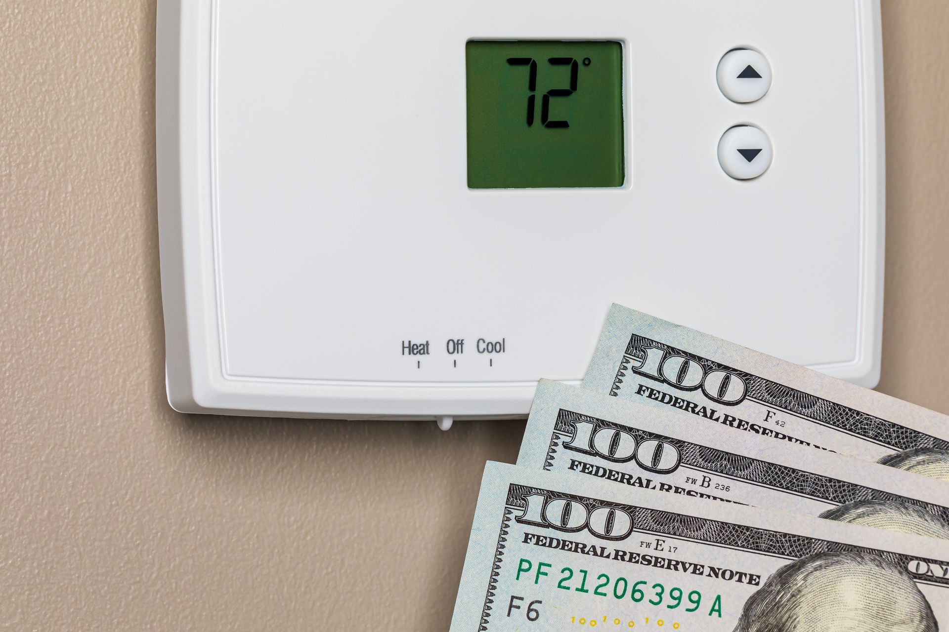 A white wall-mounted thermostat set to 72 degrees next to several hundred-dollar bills.