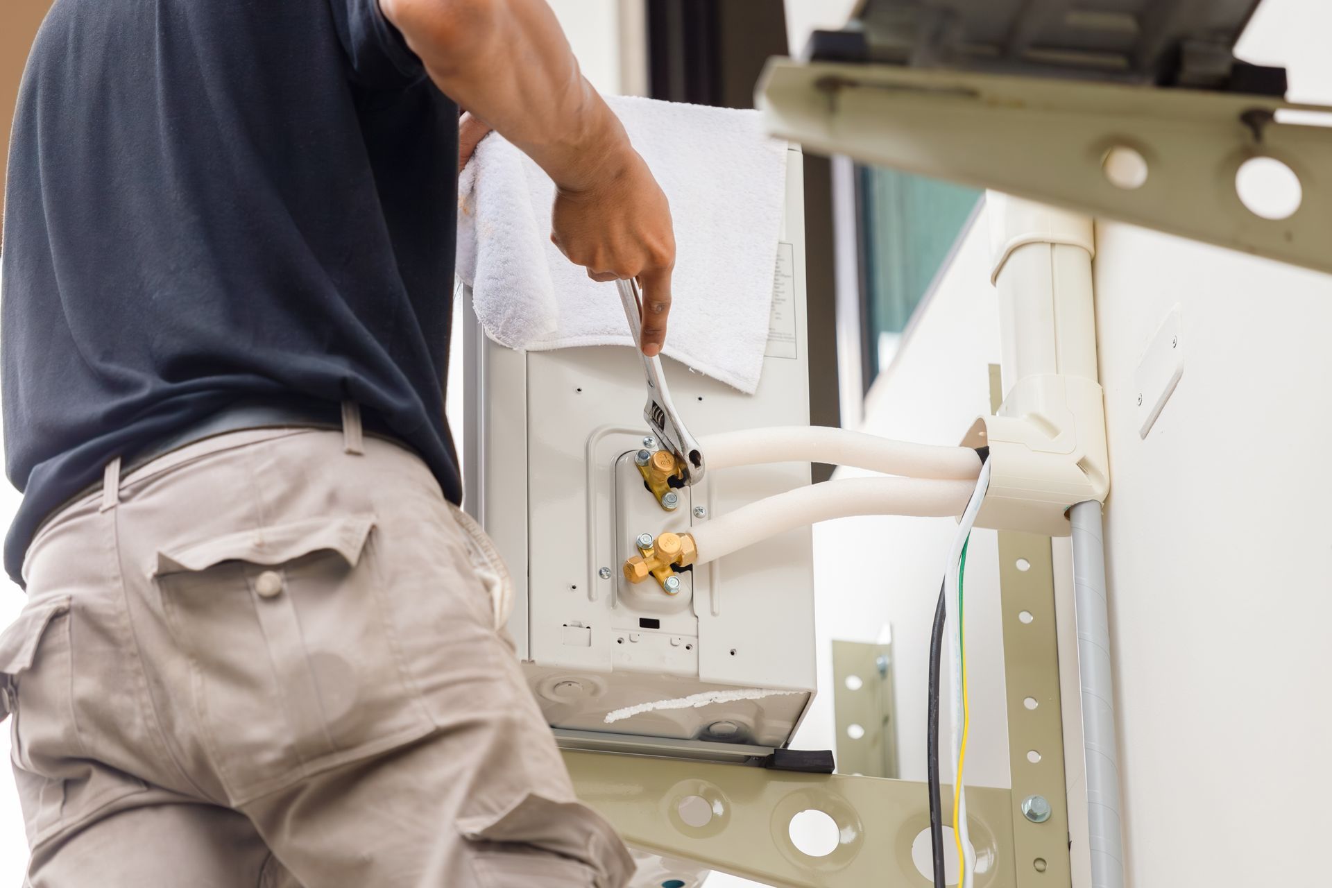 A technician uses a wrench to service the brass fittings on an outdoor air conditioning unit.