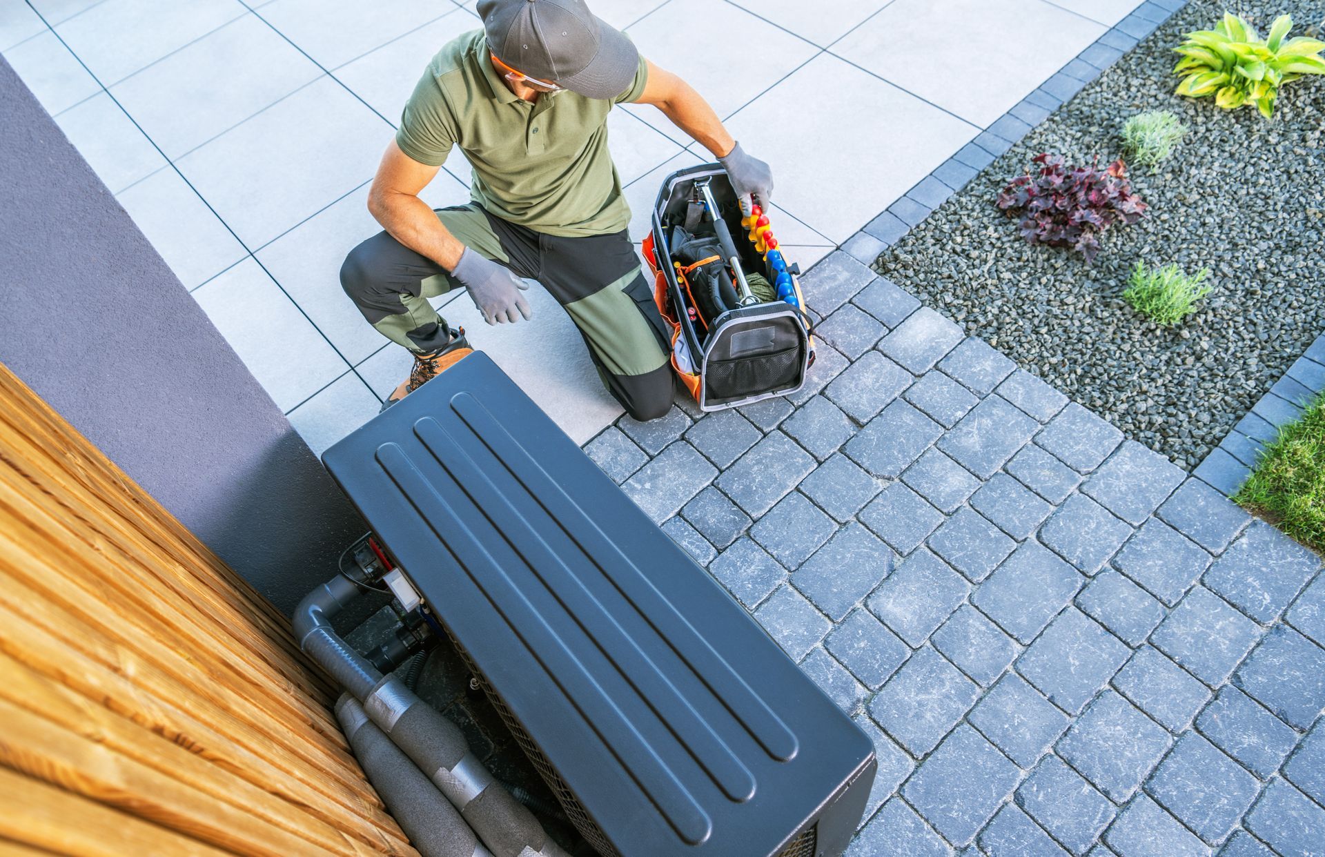 A technician uses two wrenches to tighten a metal valve fitting on an outdoor air conditioning unit.