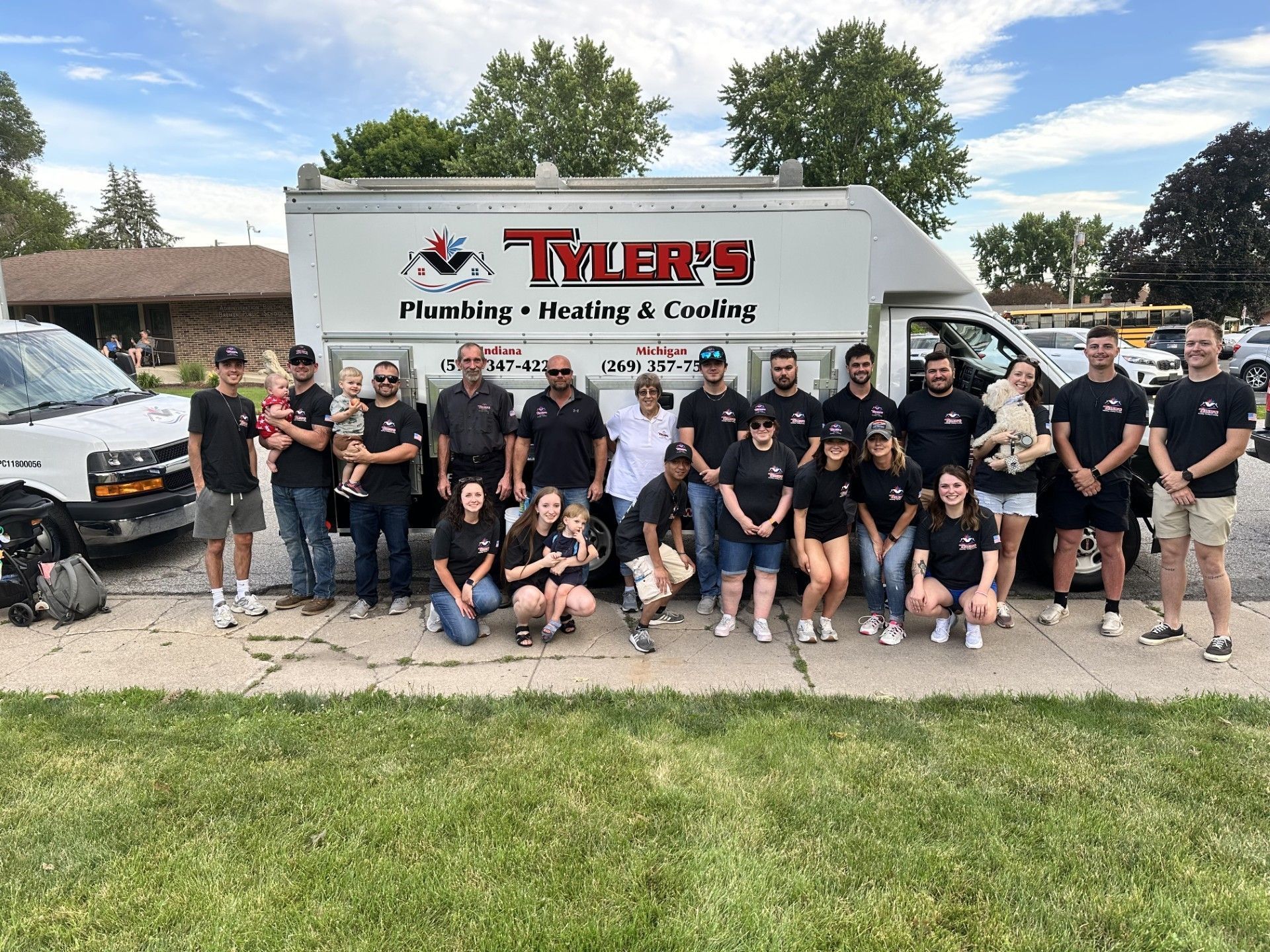 A large group of people pose in front of a Tyler's Plumbing, Heating & Cooling service truck on a sunny day.