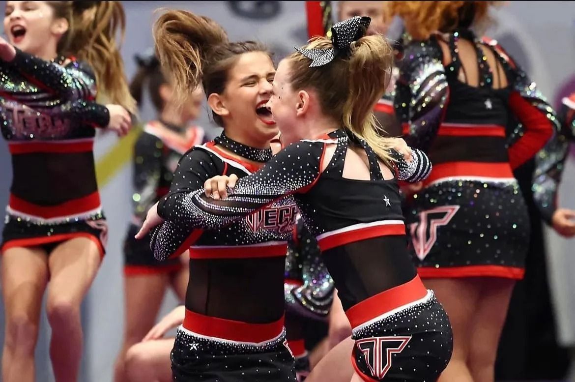 Two Cheerleaders in Black and Red Uniforms Embrace — Cedar Park, TX — Tech Cheer