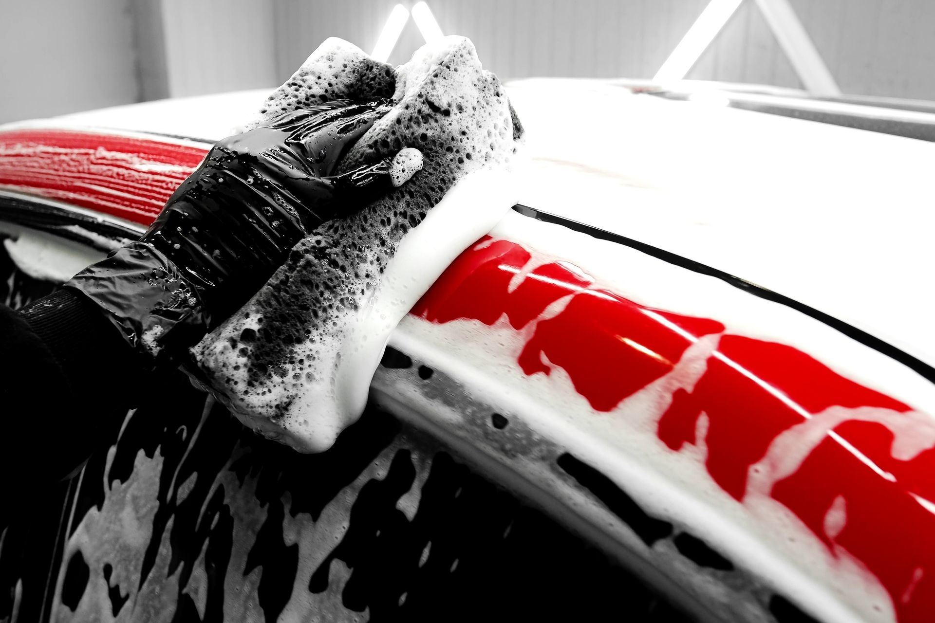 Gloved hand washing a white and red car with a soapy sponge.