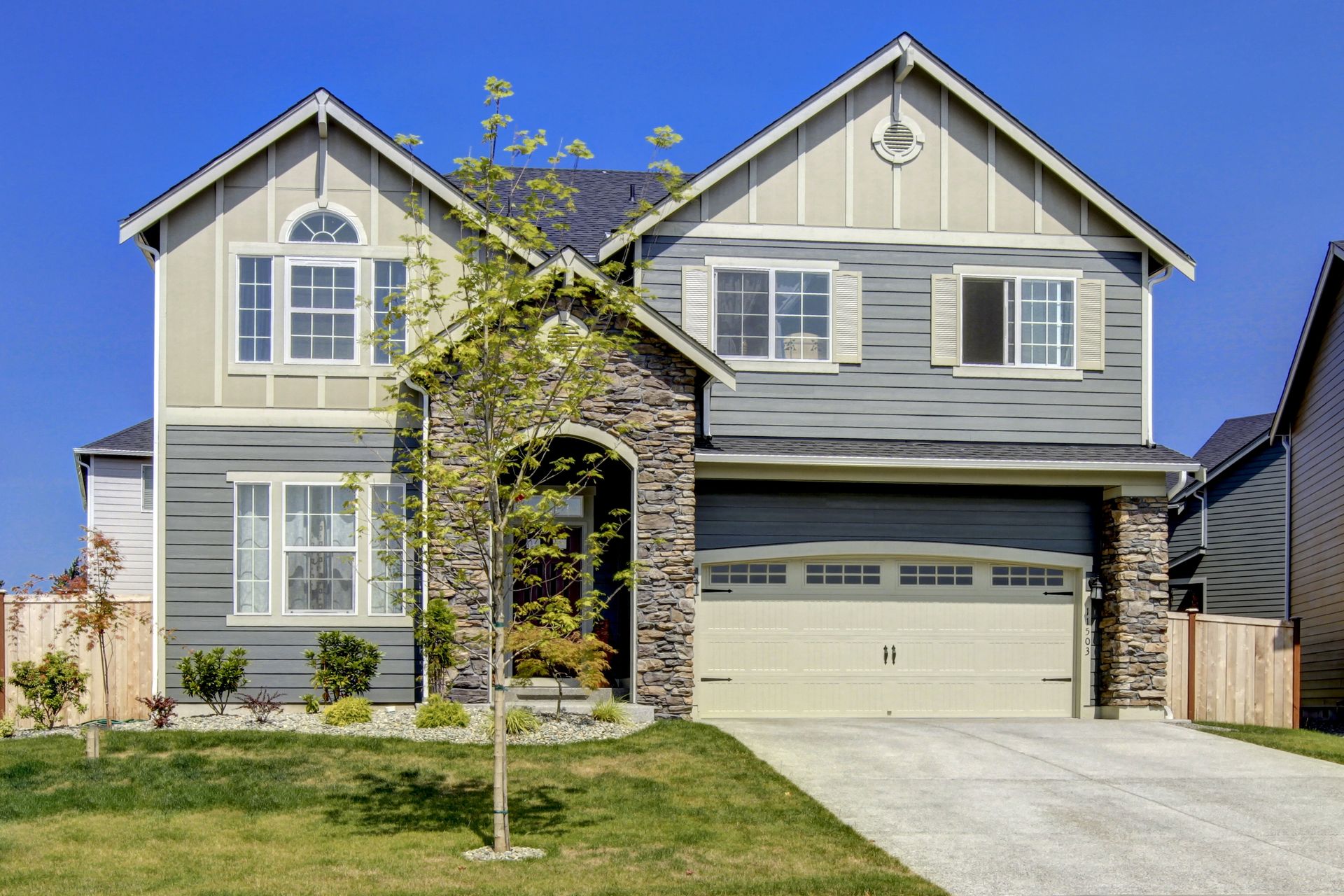 A large house with a garage and a tree in front of it.