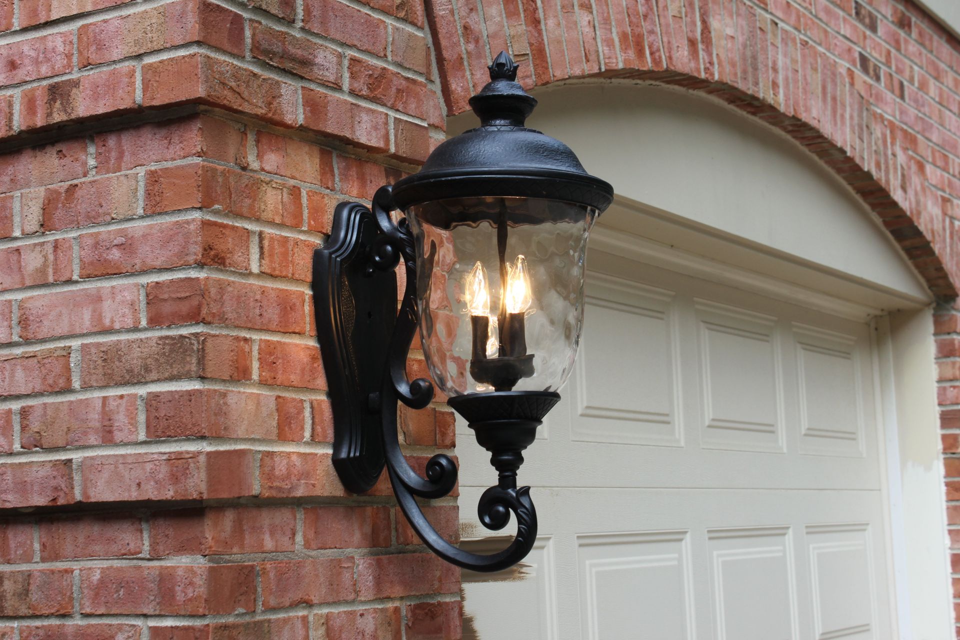 A black lantern is hanging on a brick wall next to a garage door.