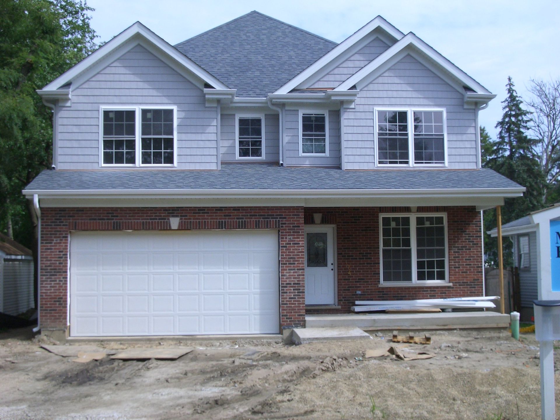 A brick house with a white garage door and a for sale sign in front of it