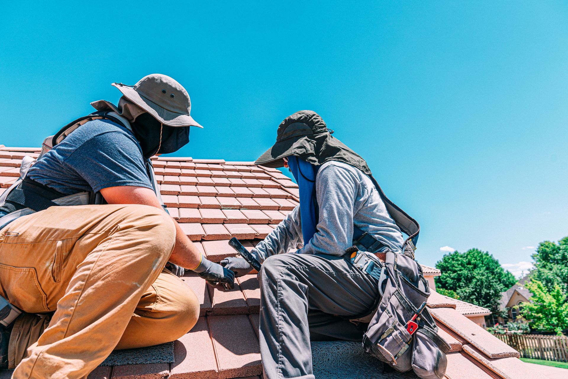 Two men performing roofing repairs on a house, using tools and safety gear for maintenance work.