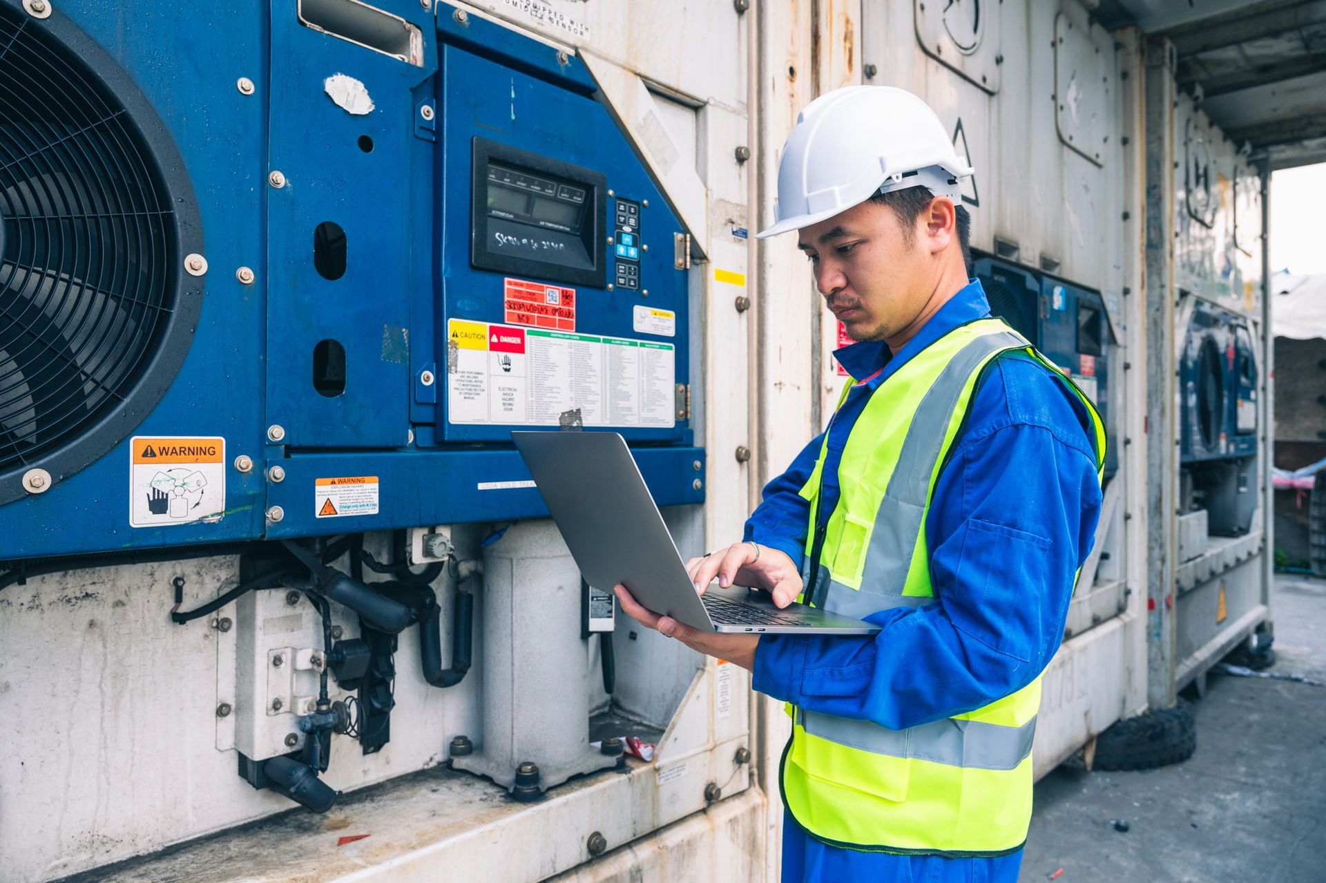 Male worker in hard hat doing commercial refrigeration repair and system testing with laptop.