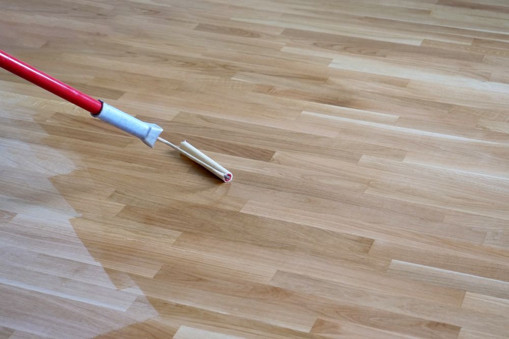 Red and white handled tool touching a light brown wooden floor.