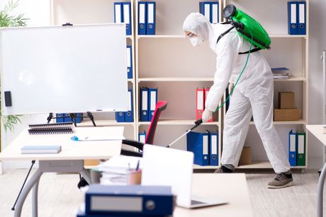 Person in protective suit spraying disinfectant in an office.