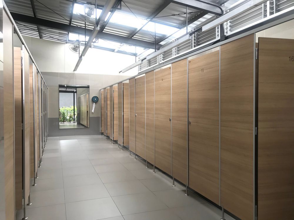 Long hallway of public restroom stalls with light wood doors and a tile floor.