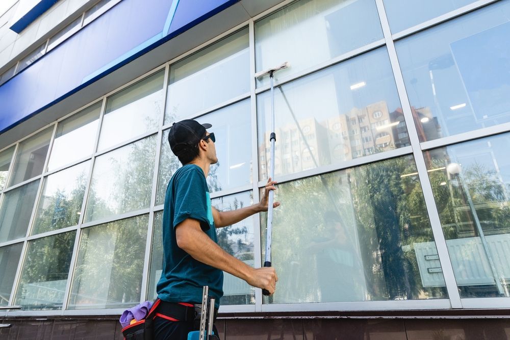 Person washing large commercial building windows with a long-handled squeegee.