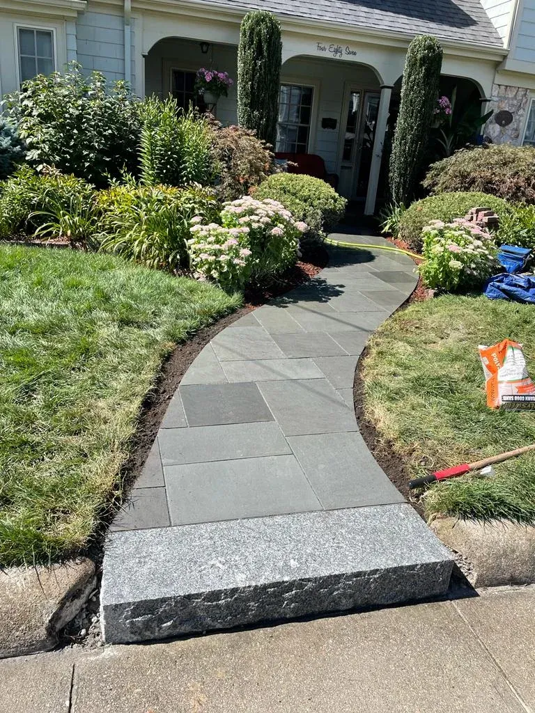 A new stone walkway leads to a front door, featuring a grey granite step at the bottom and landscaping on both sides.