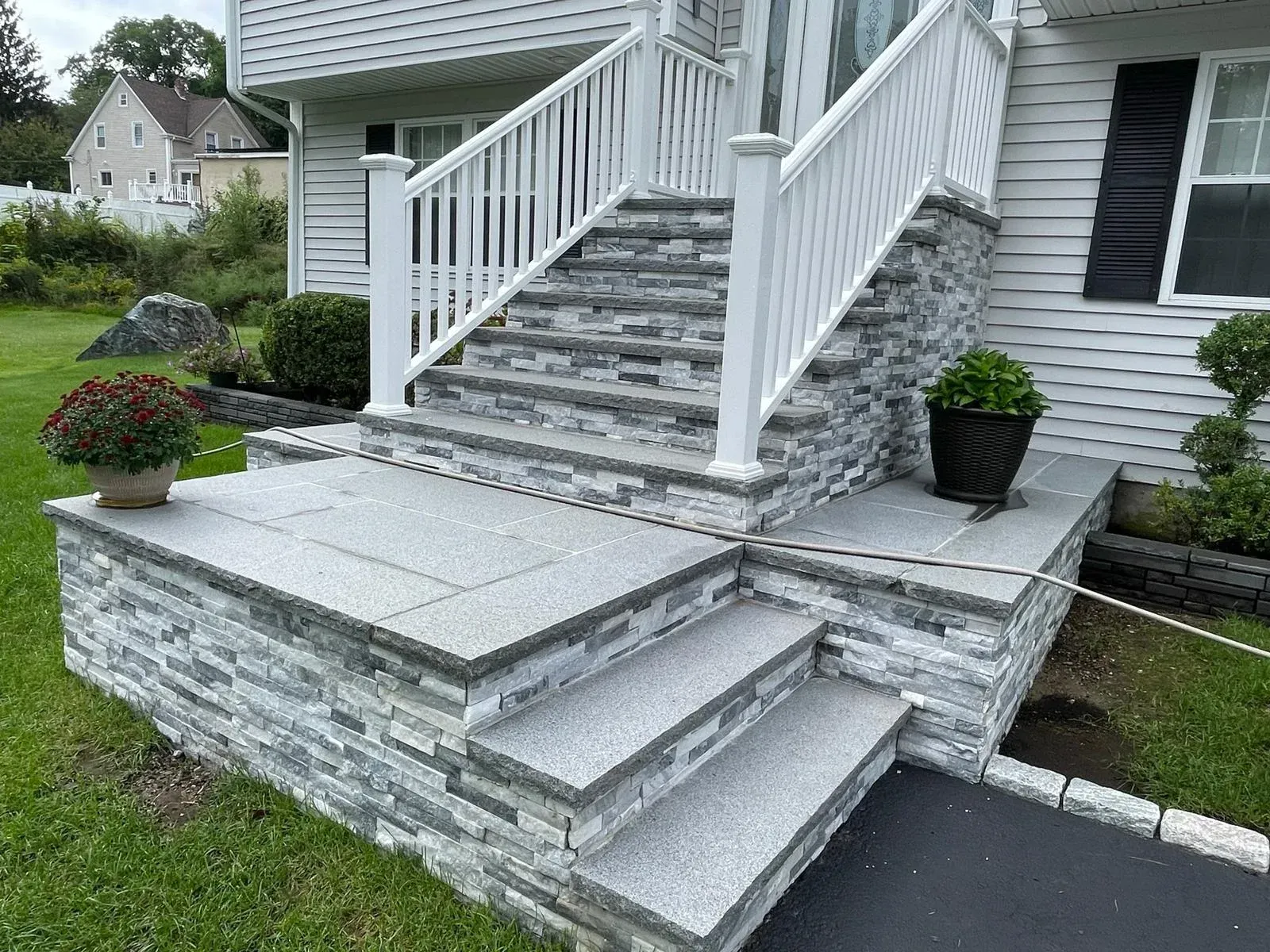 Front exterior view of a grey stone staircase and landing with white railings leading to a residential entrance.