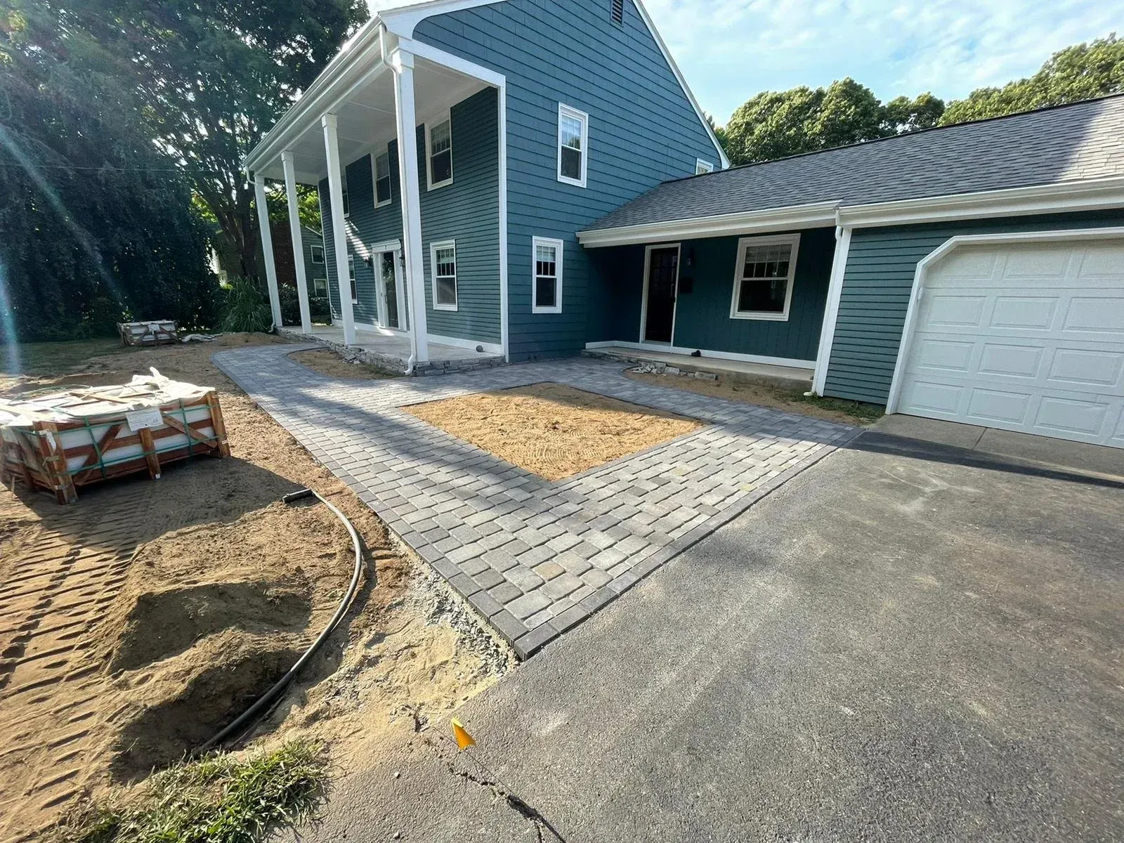 A teal two-story home with a newly installed gray paver walkway leading to the front porch and a side garage.