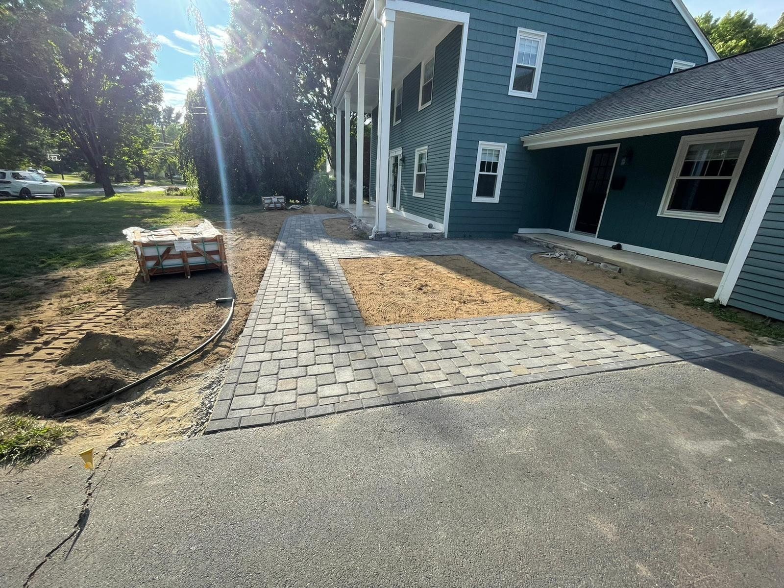 A blue house with a new brick walkway and driveway section under construction on a sunny day.
