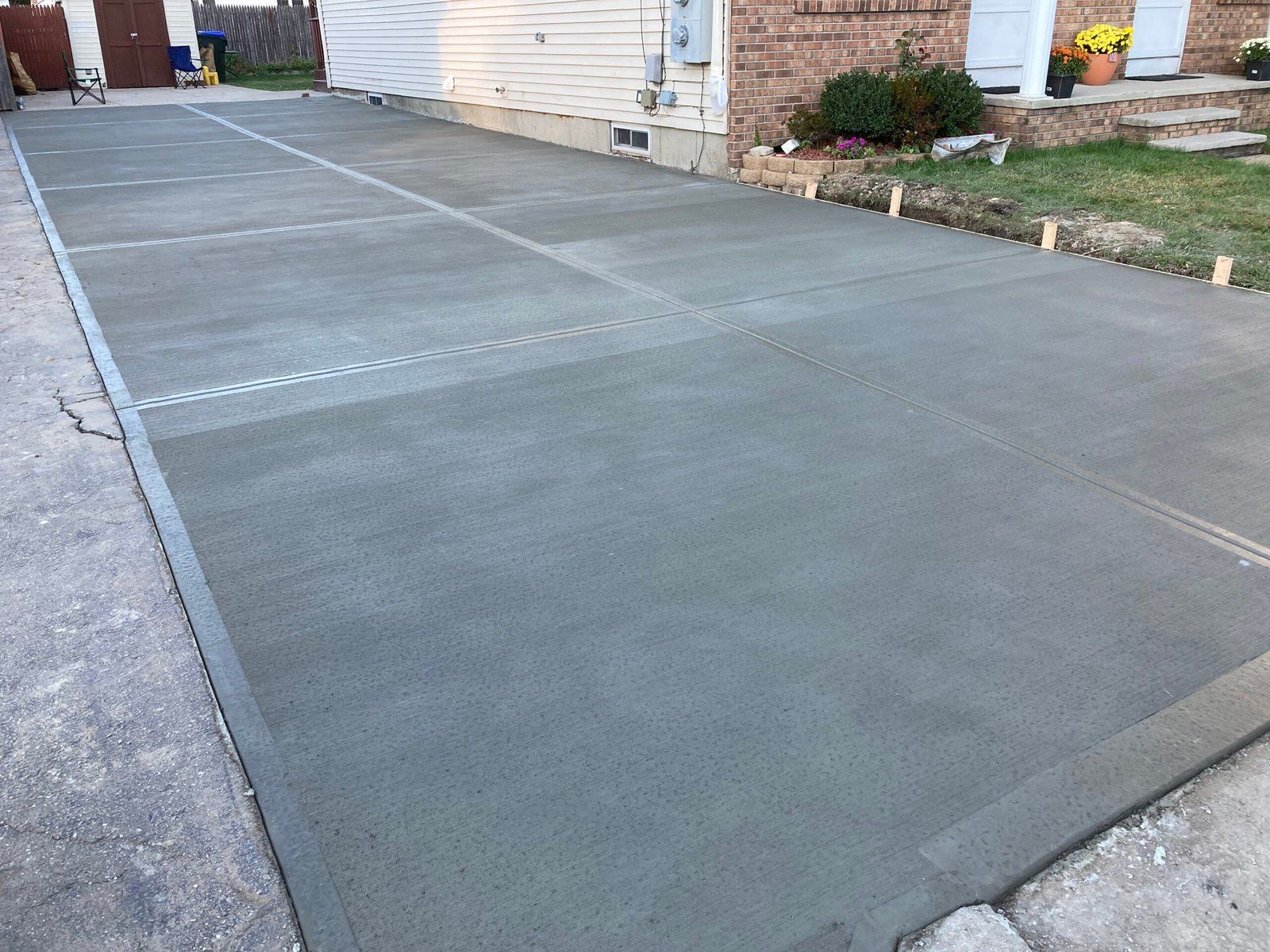 A freshly poured rectangular concrete driveway extension positioned next to a house with light siding and a brick stoop.