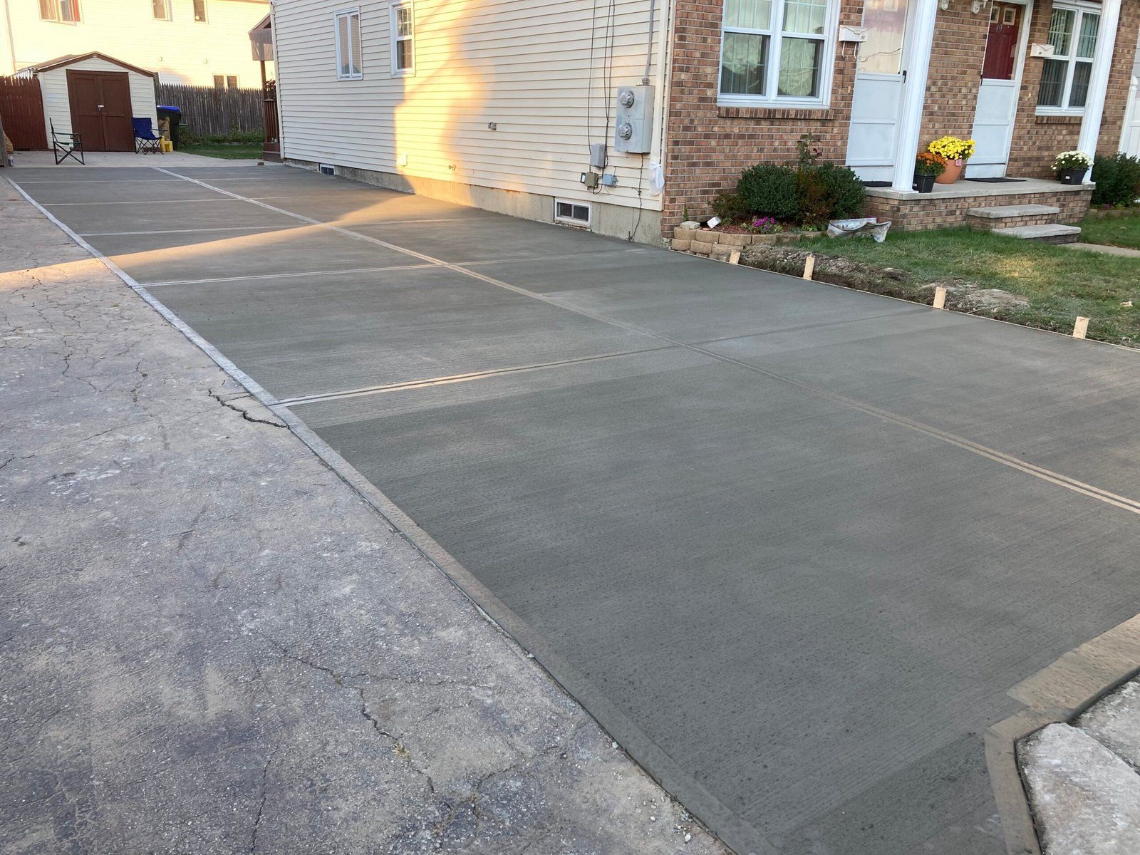 A new concrete driveway section adjacent to an older, weathered asphalt driveway leading to a house.