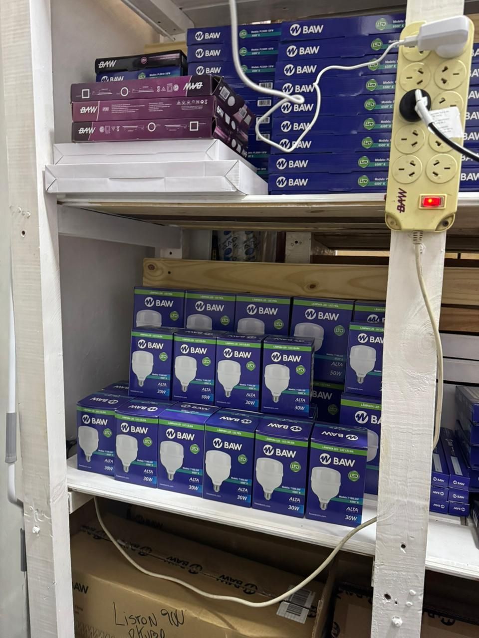 Estanterías repletas de cajas de bombillas azules y blancas, regleta de enchufes enchufada.