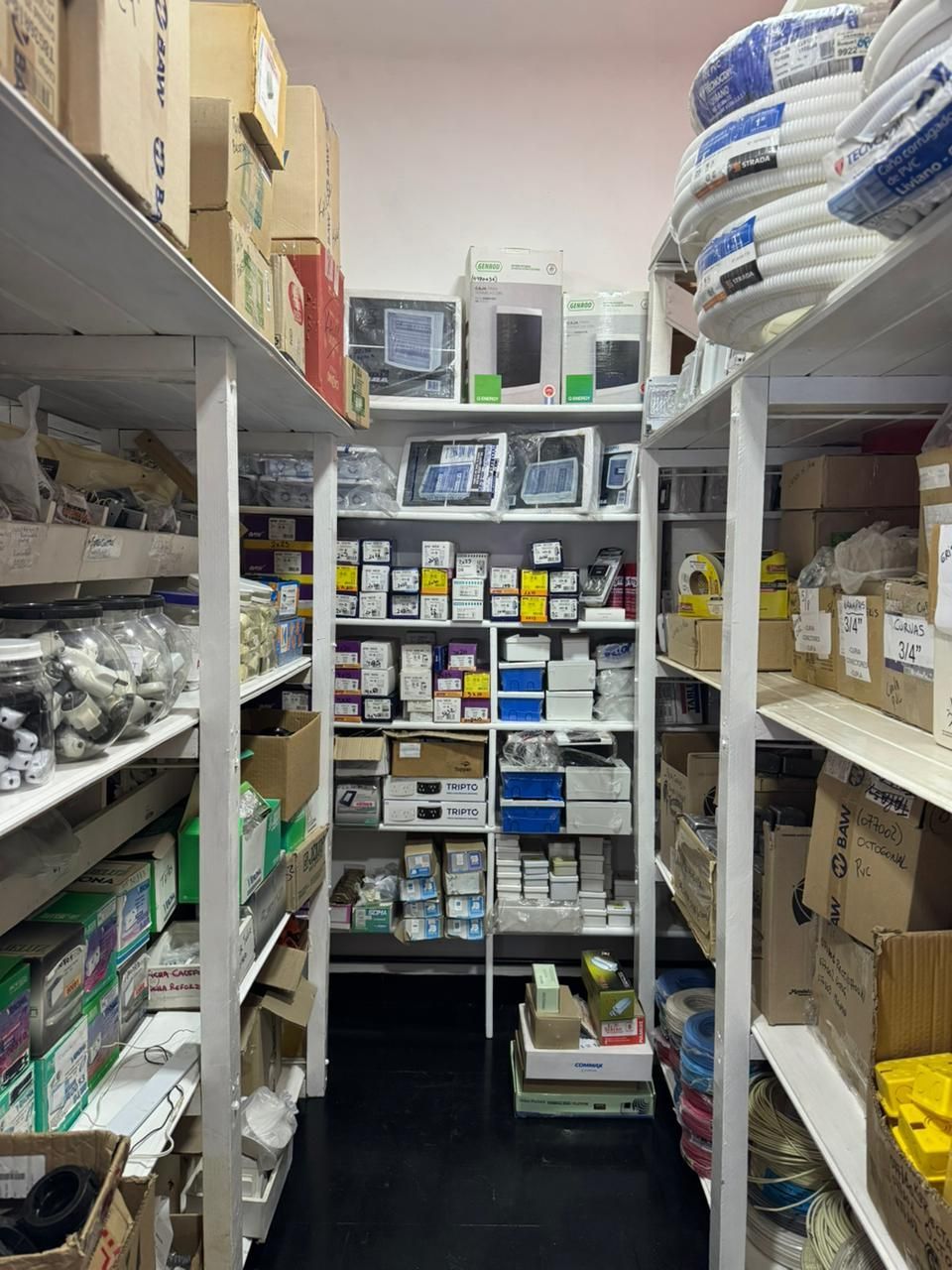 Estanterías repletas de diversos artículos en cajas en un trastero con soportes metálicos blancos.