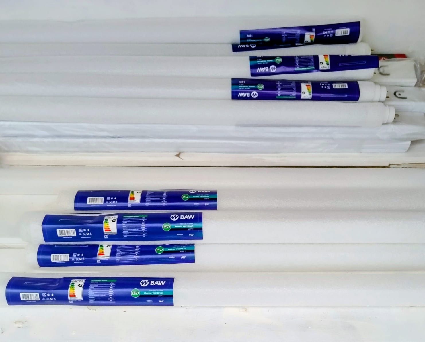 Varios tubos fluorescentes blancos y largos en un estante. Cada tubo está en su caja original.