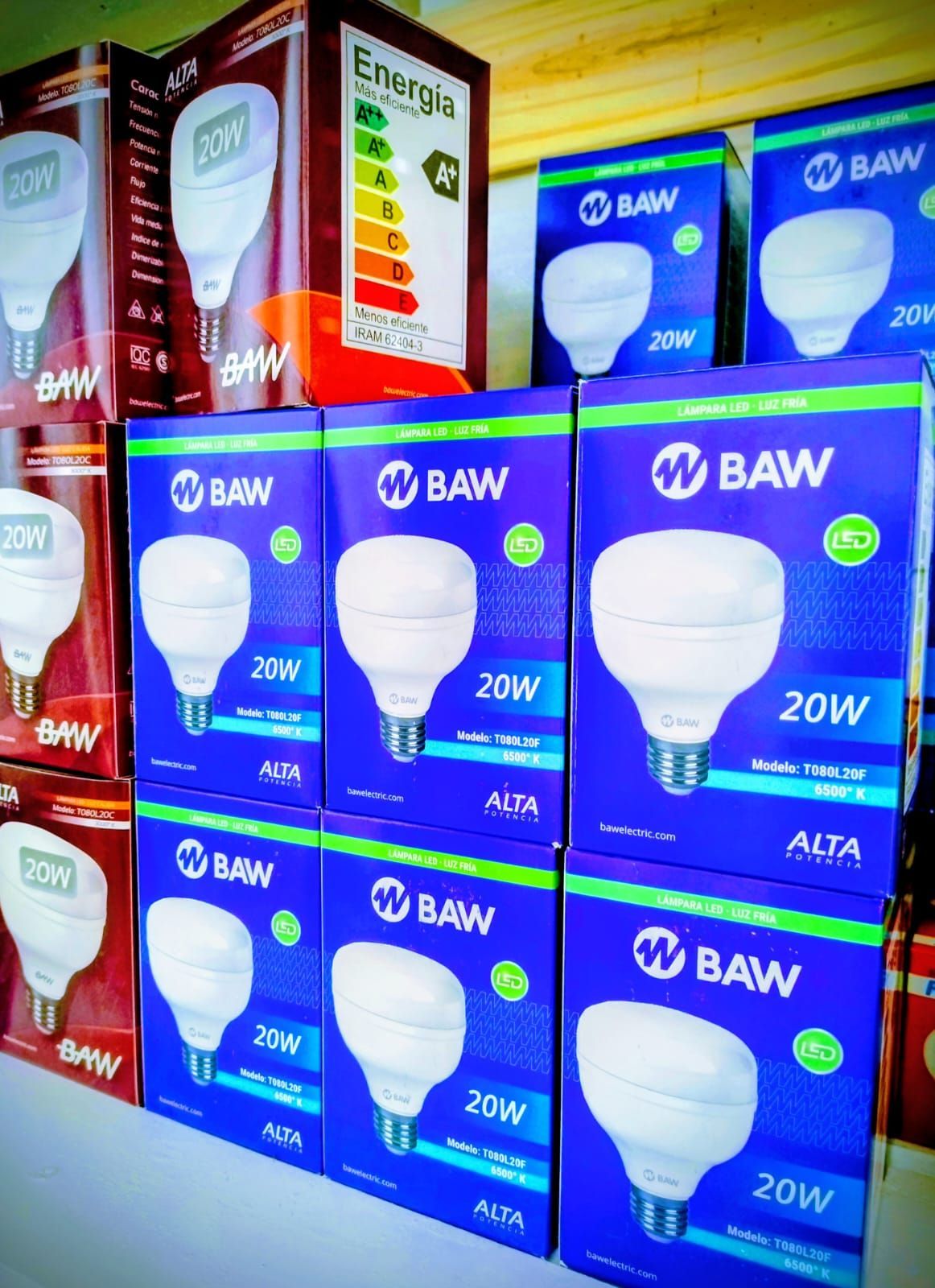 Filas de bombillas BAW de 20 W en cajas azules, apiladas en un estante. Se puede ver la tabla de clasificación energética.